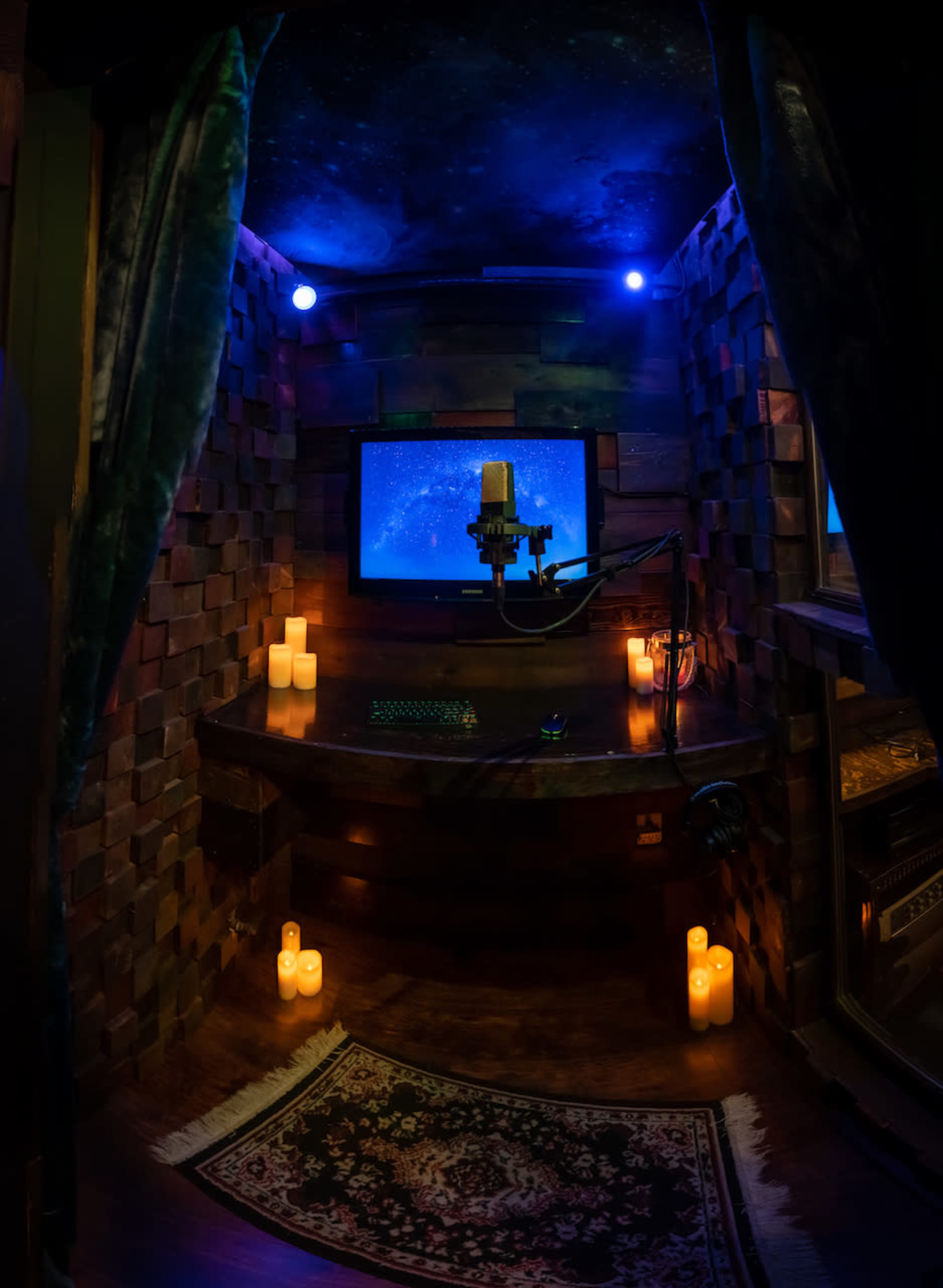 A small recording booth features a desk with a computer monitor and microphone, surrounded by dim lighting and candles.