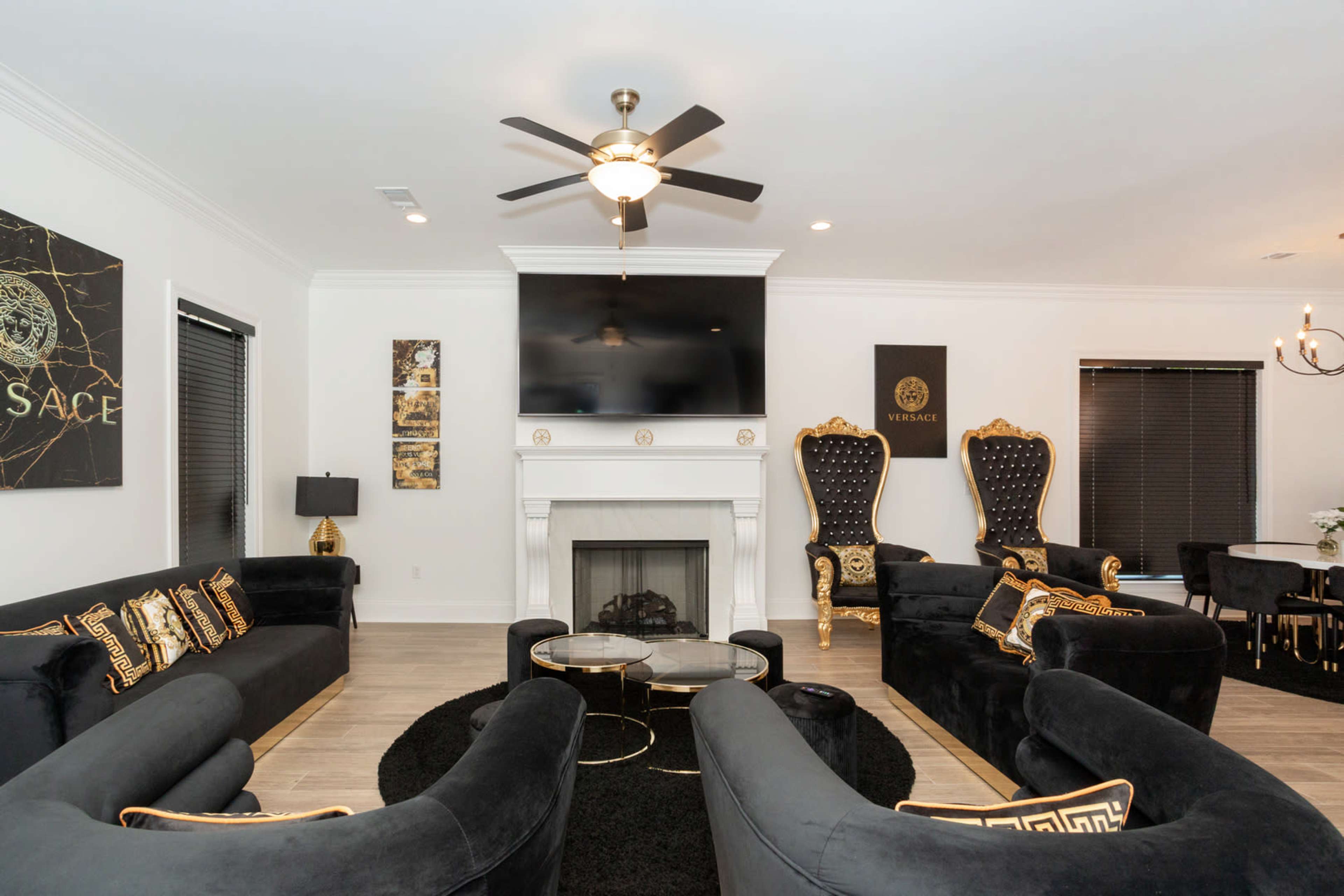 A modern living room featuring black velvet sofas with gold accents, a fireplace, a large wall-mounted television, and elegant decorative elements.