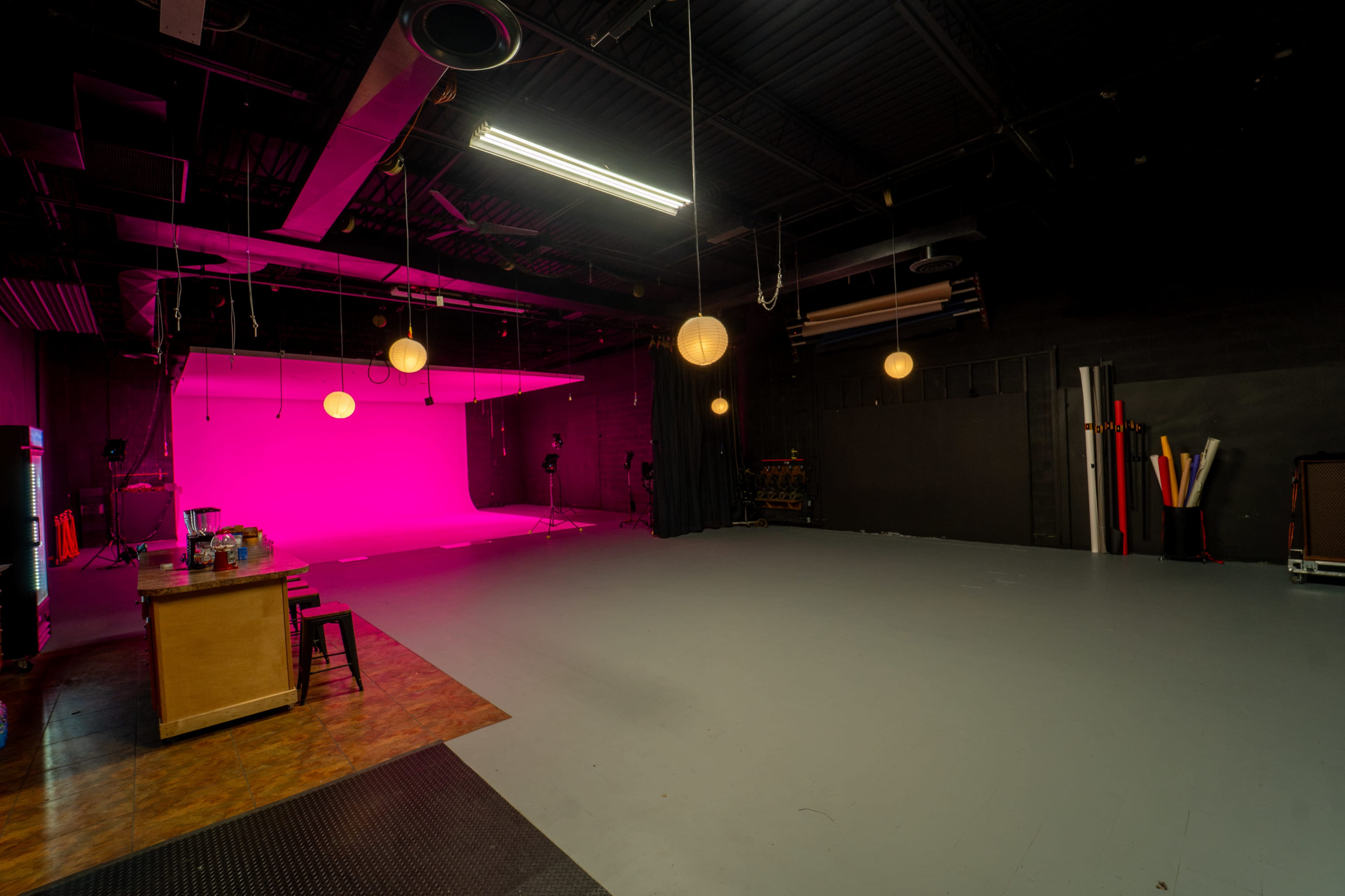 The image shows a spacious photography studio with a pink backdrop, dim lighting, and various studio equipment in the corners.