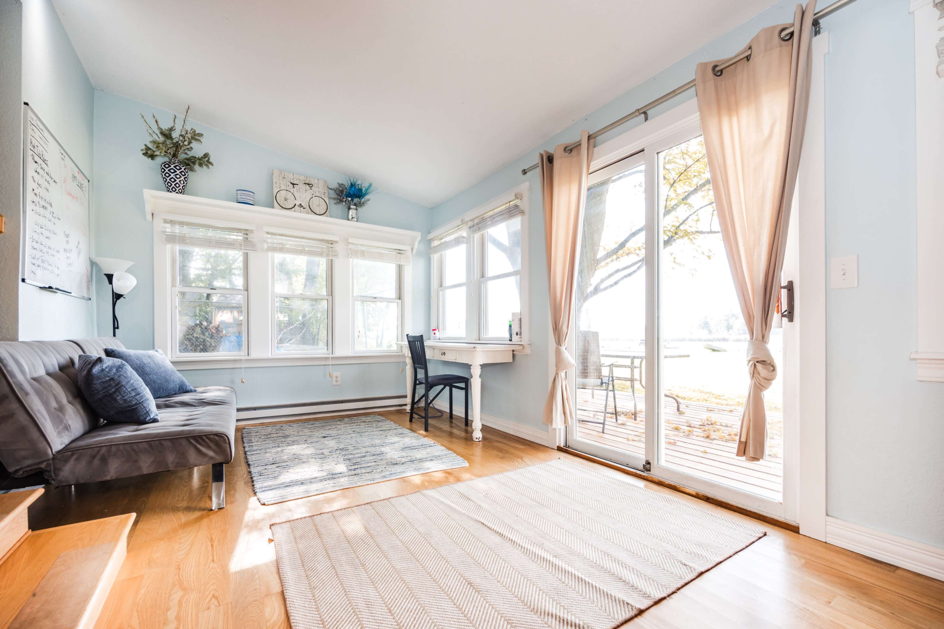 The image shows a bright, airy room featuring a couch, a small desk by the window, and large glass doors leading to an outdoor area.