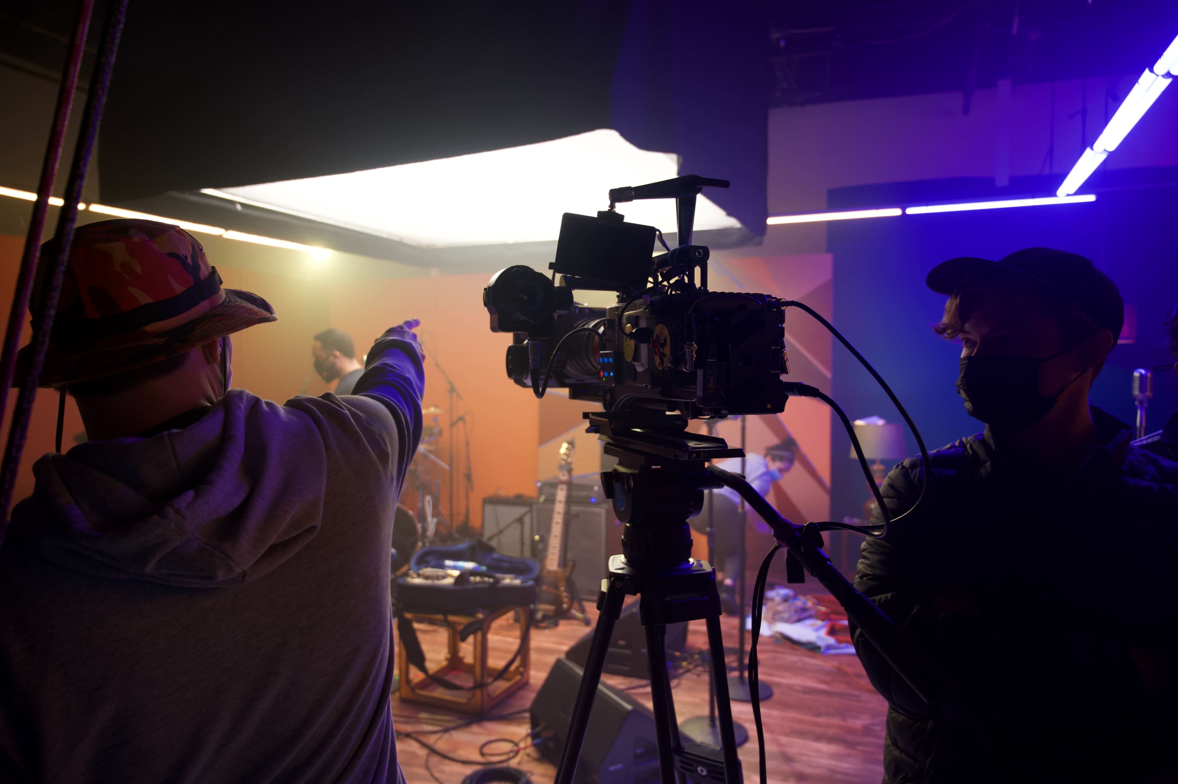 A film crew sets up equipment in a studio, with one crew member pointing while another operates a camera.