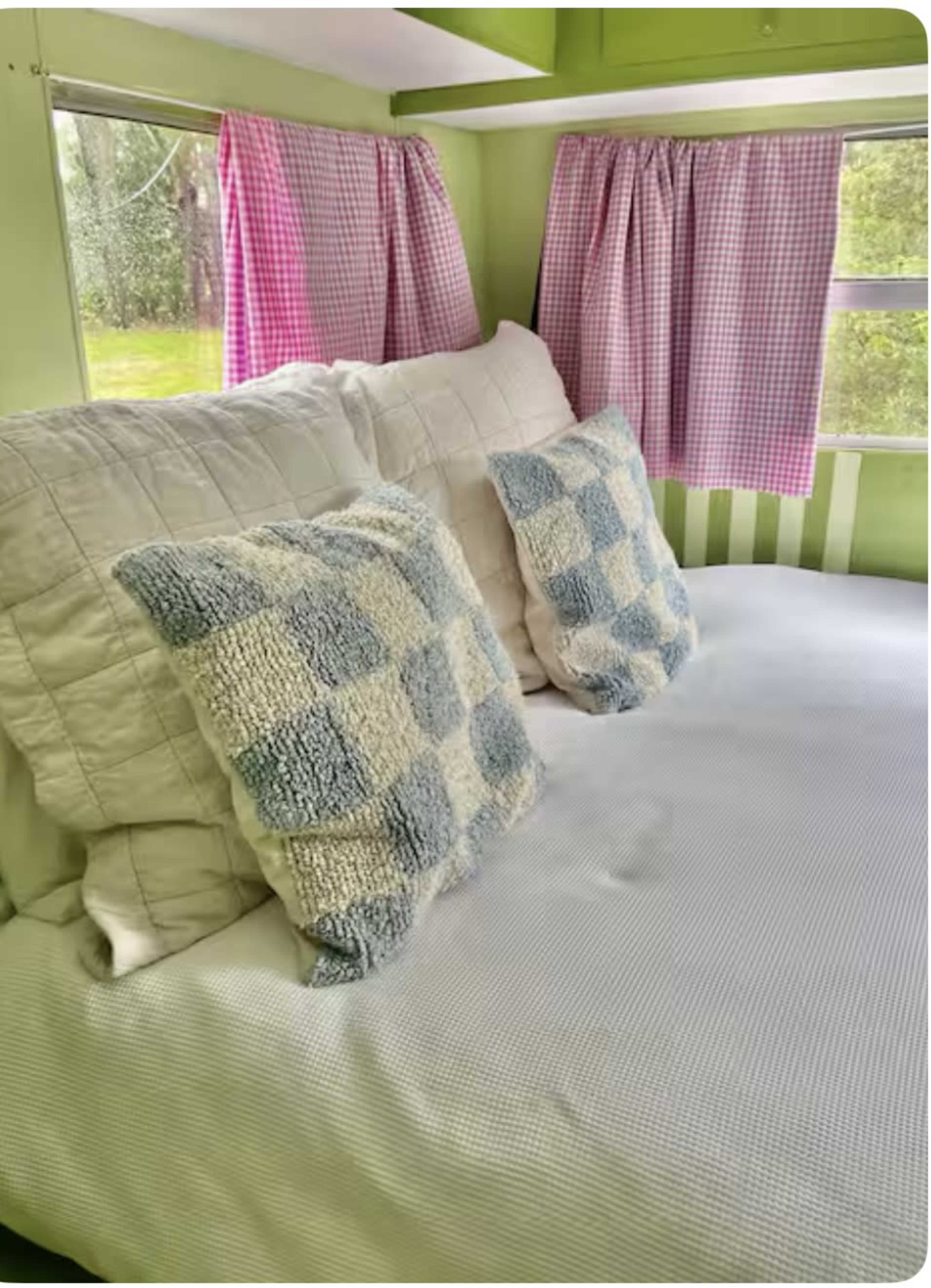 The image shows a bed with white bedding and two checkered pillows situated against a green wall with checkered curtains at the windows.