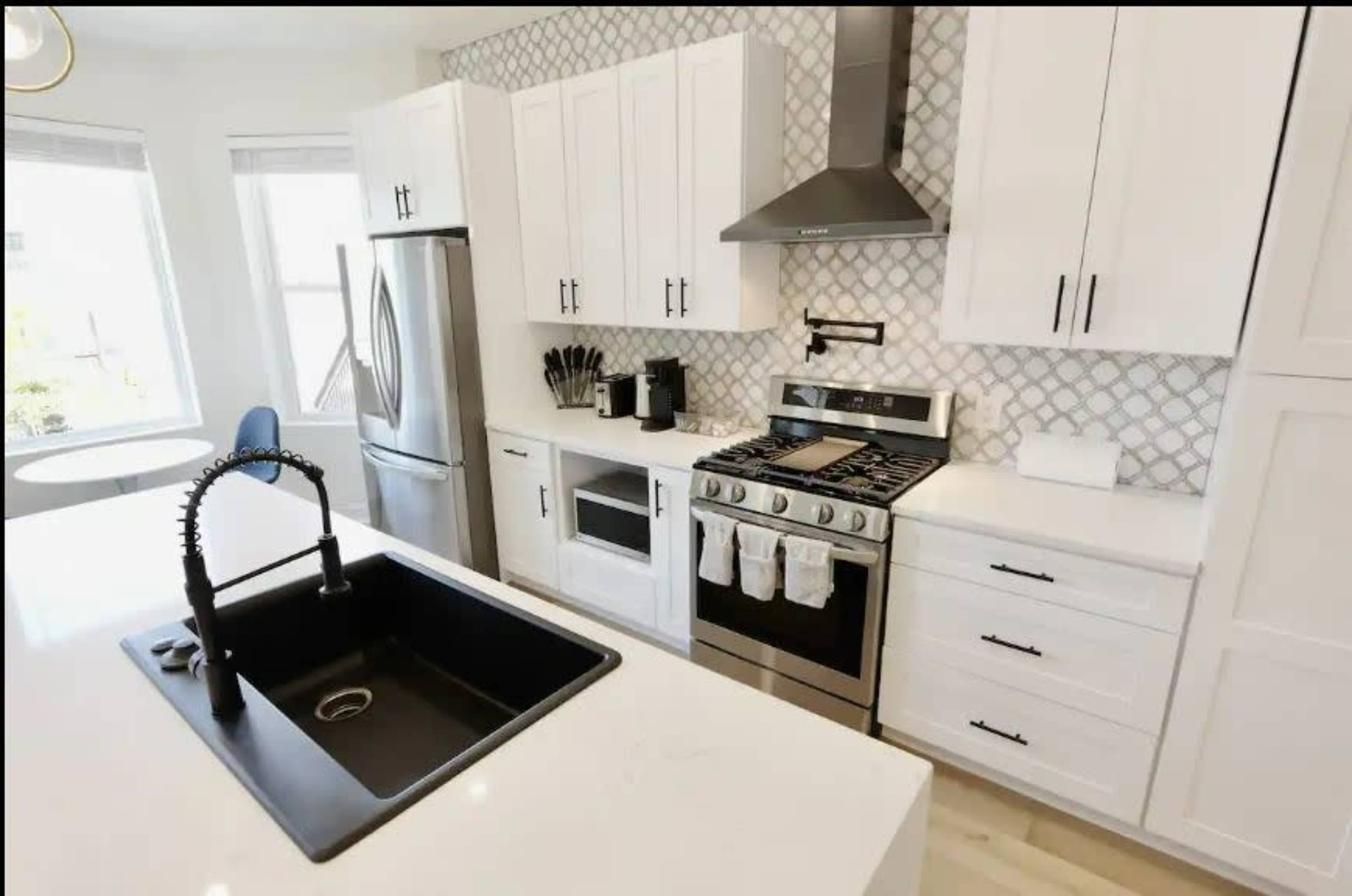 The modern kitchen features white cabinets, a stainless steel refrigerator, a black sink, and a gas stove with a decorative backsplash.