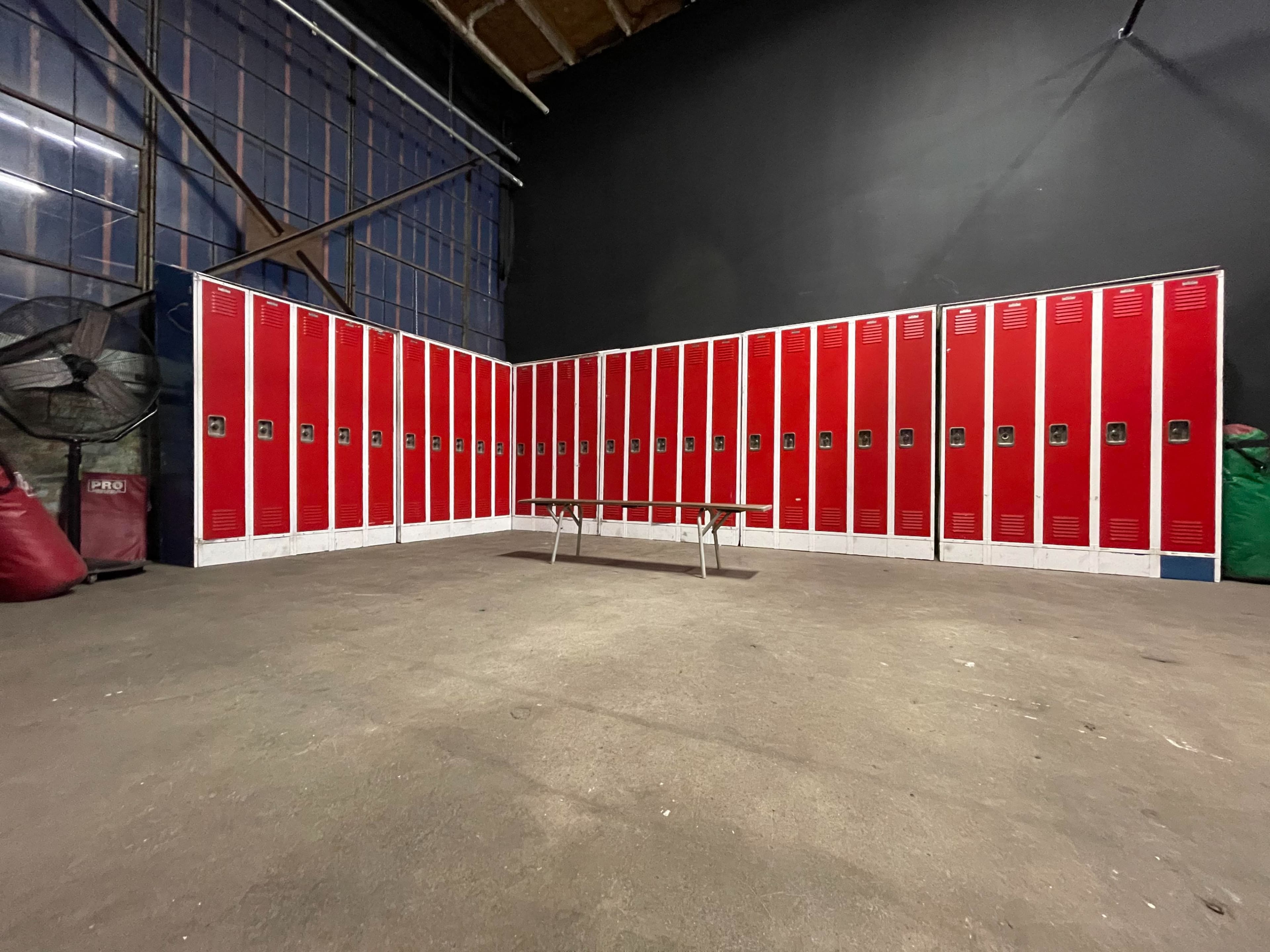 The image depicts a row of red lockers against a black wall in a spacious, industrial setting.