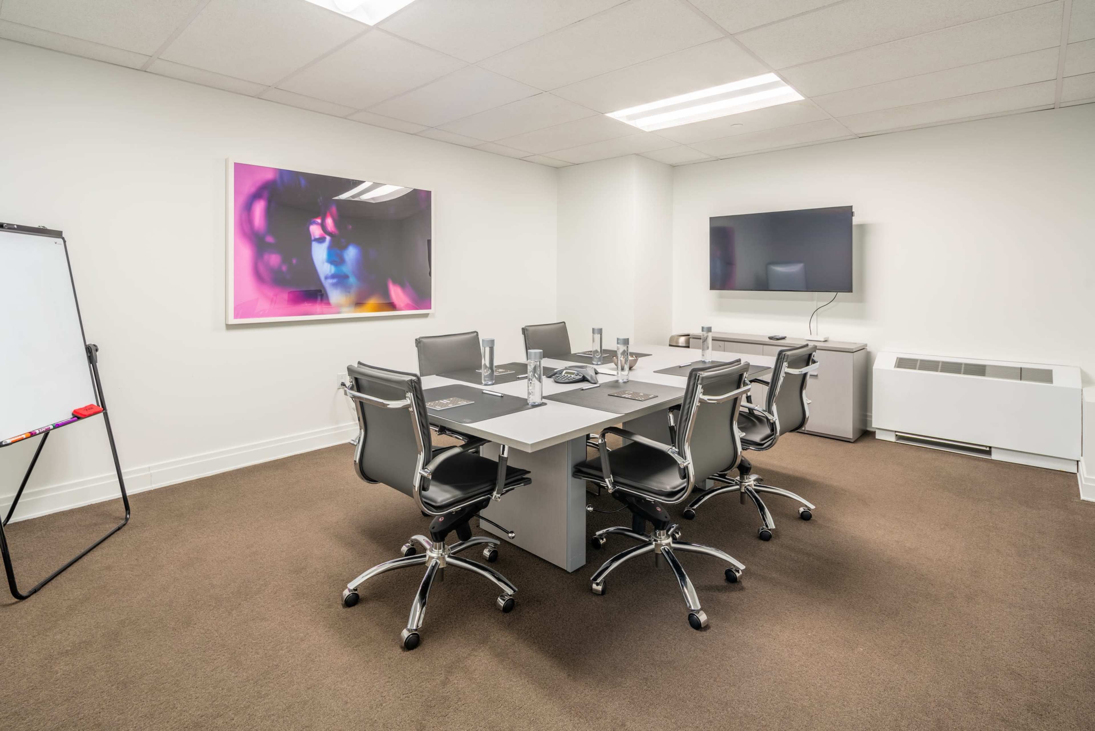 A modern conference room with a rectangular table surrounded by six chairs, a whiteboard, and a television mounted on the wall.