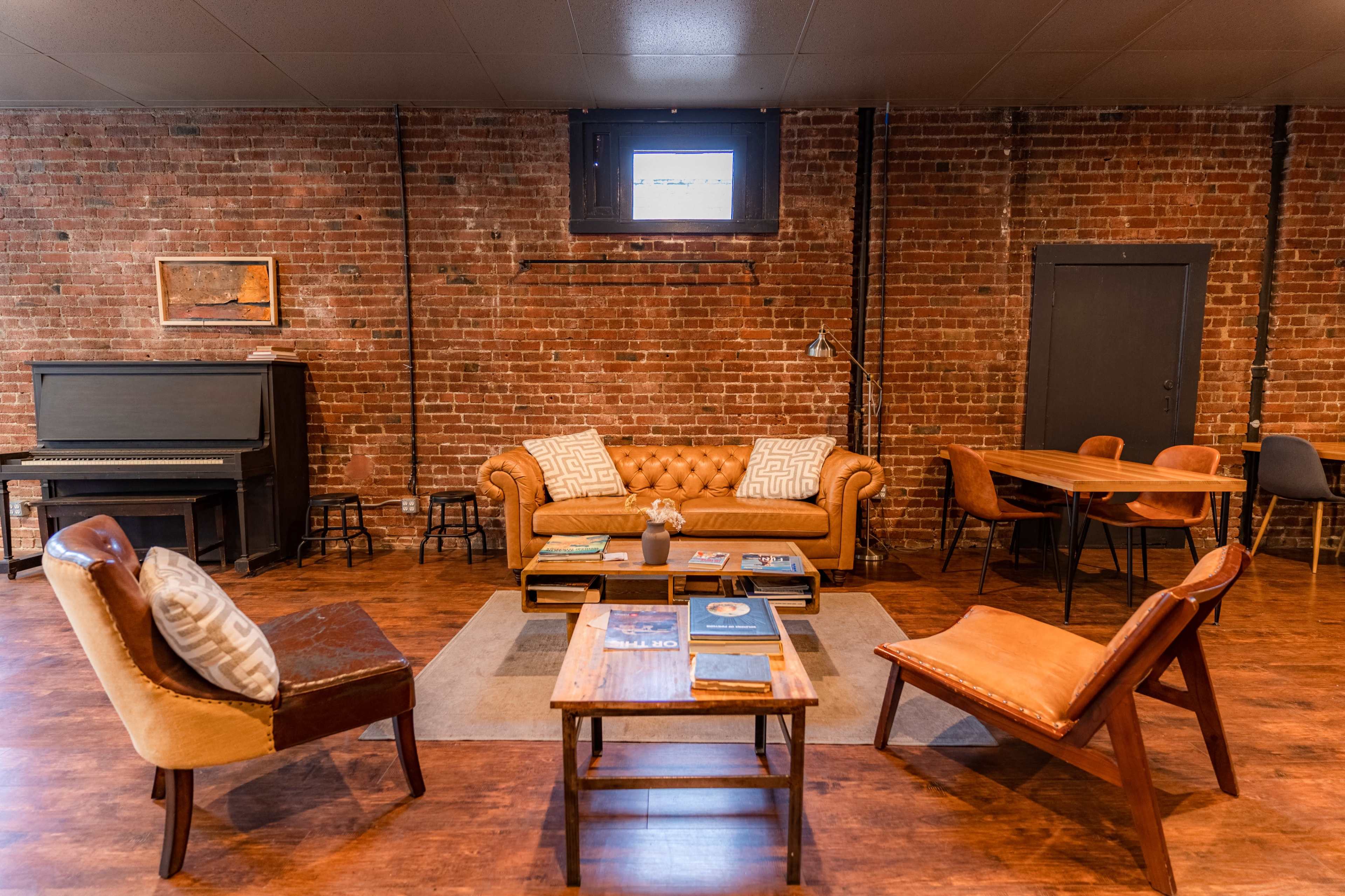 A cozy lounge area with a leather sofa, a wooden coffee table, and various seating options, against a backdrop of exposed brick walls.