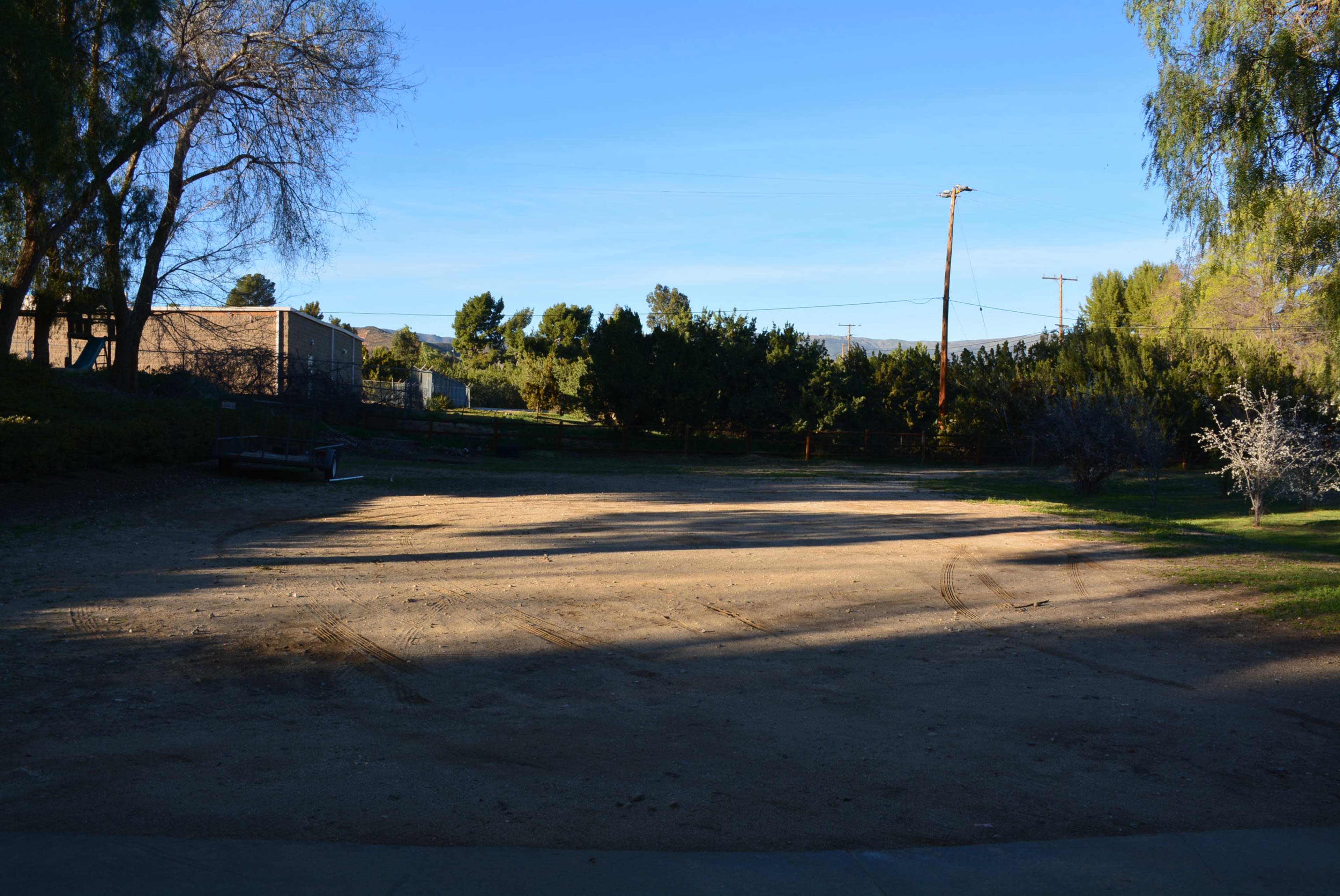 The image shows a cleared dirt area surrounded by trees and shrubs under a clear blue sky.