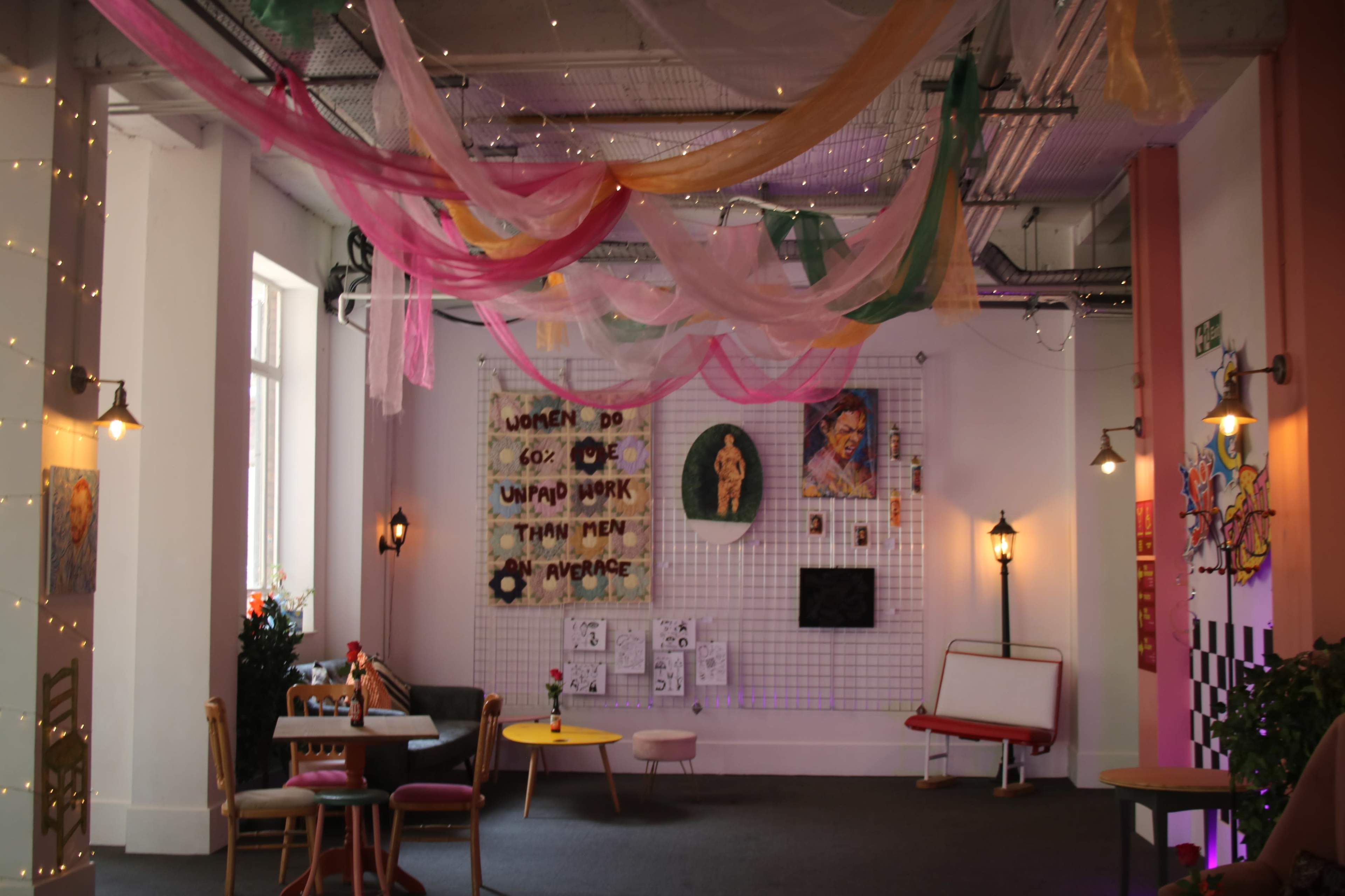 The image shows a colorful interior space with draped fabrics overhead, a wall decorated with art pieces, and various seating arrangements.