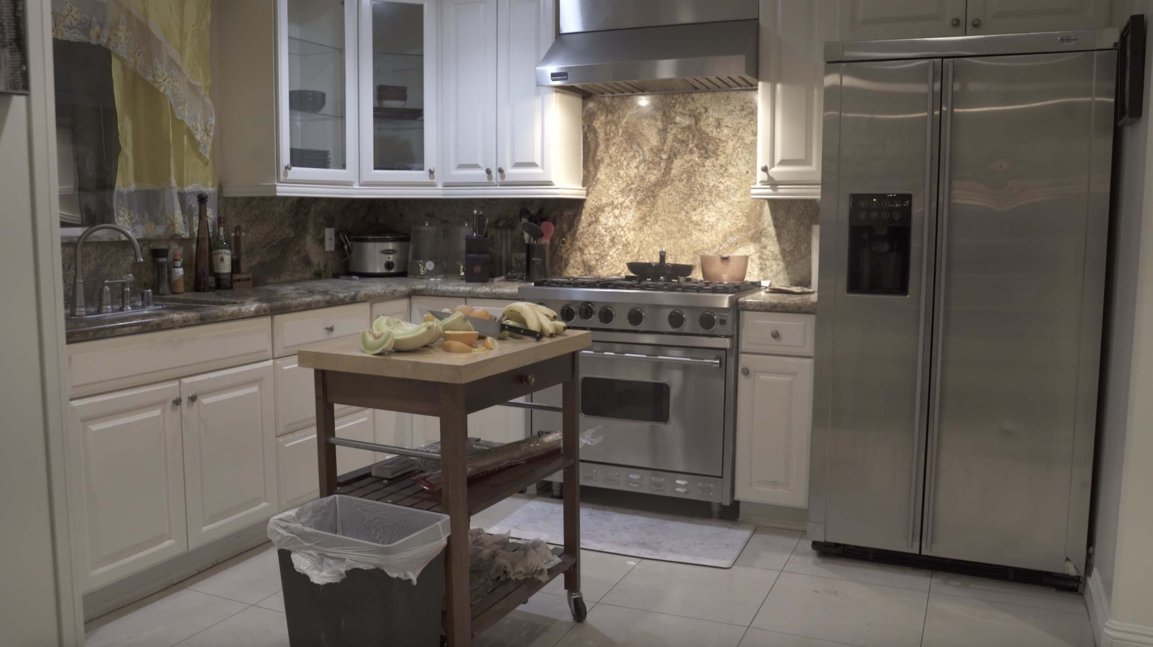 A kitchen with white cabinets, a large stainless steel refrigerator, and a wooden island displaying cut fruit.