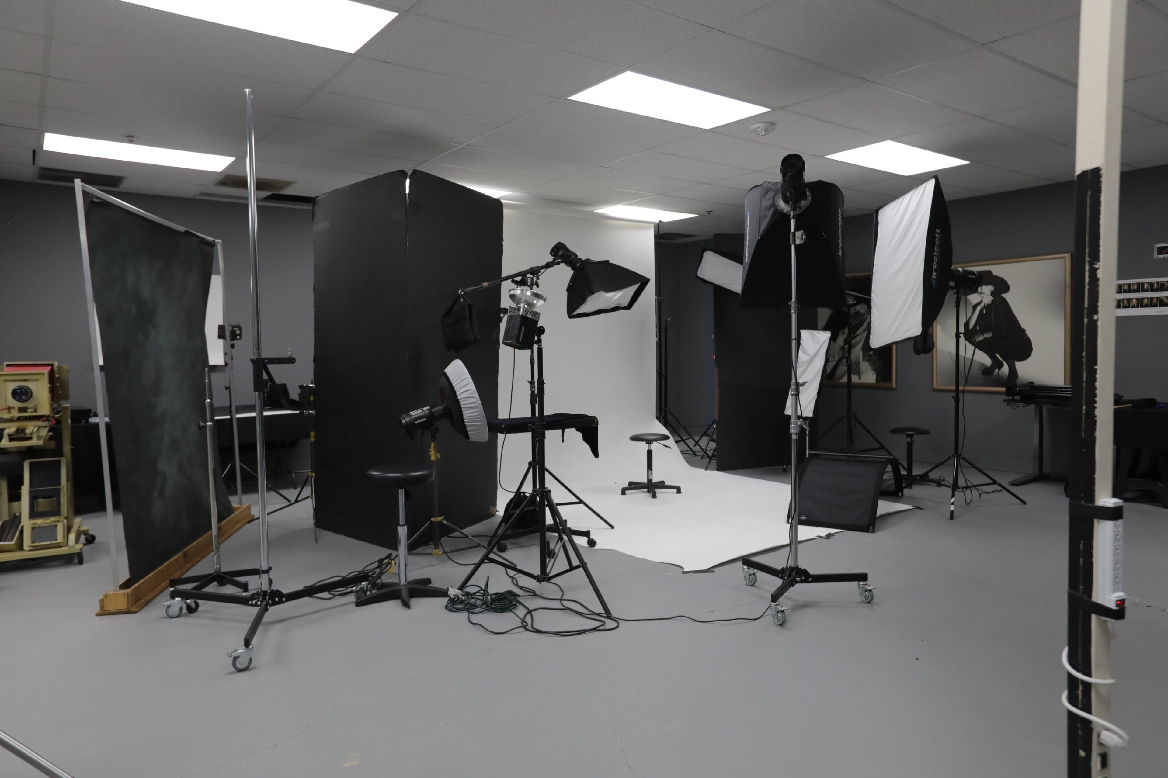 A photography studio setup with various backdrops, softboxes, and lighting equipment arranged around a central white backdrop.