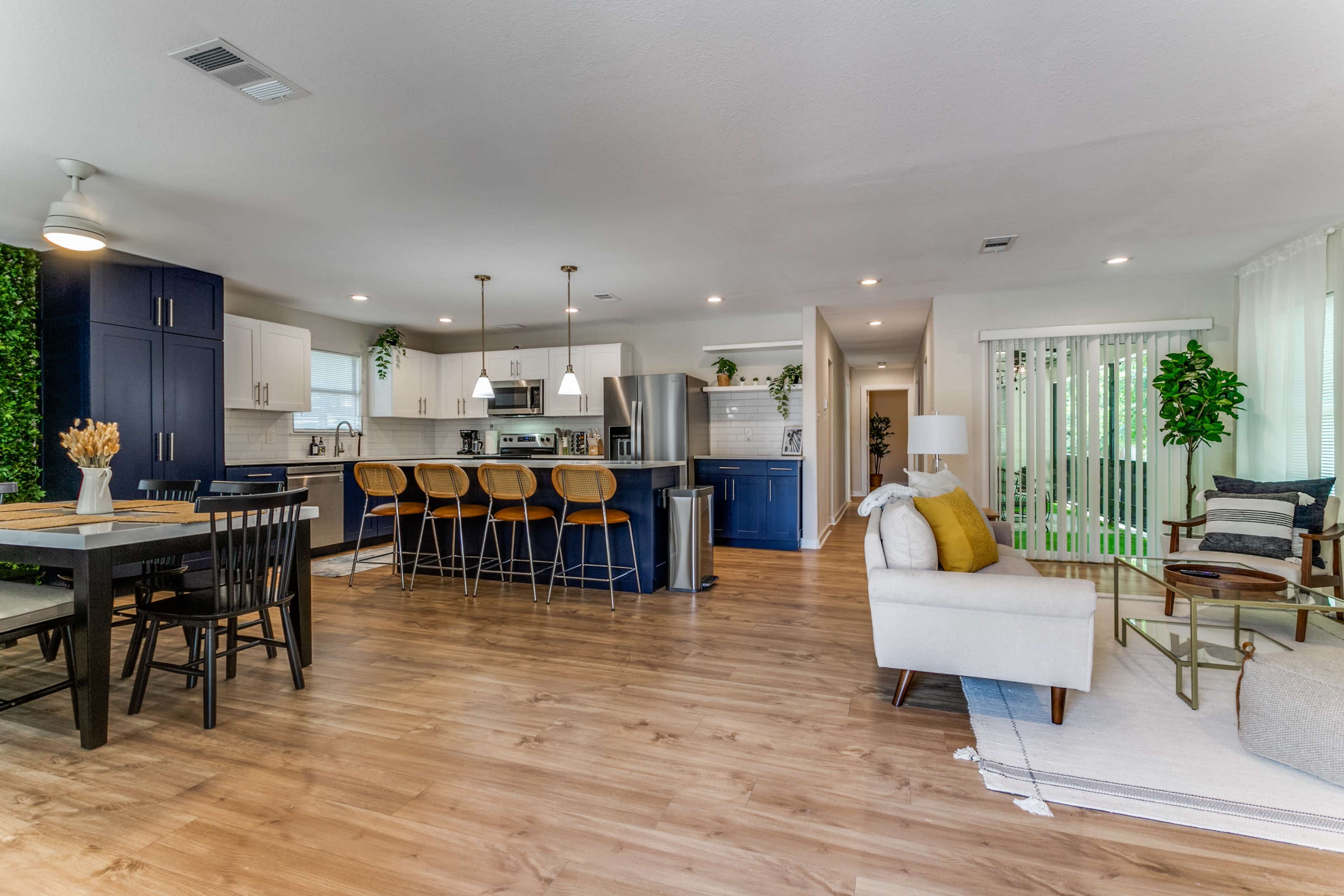 A modern open-concept kitchen and living area with dark blue cabinets, wooden flooring, and various indoor plants.