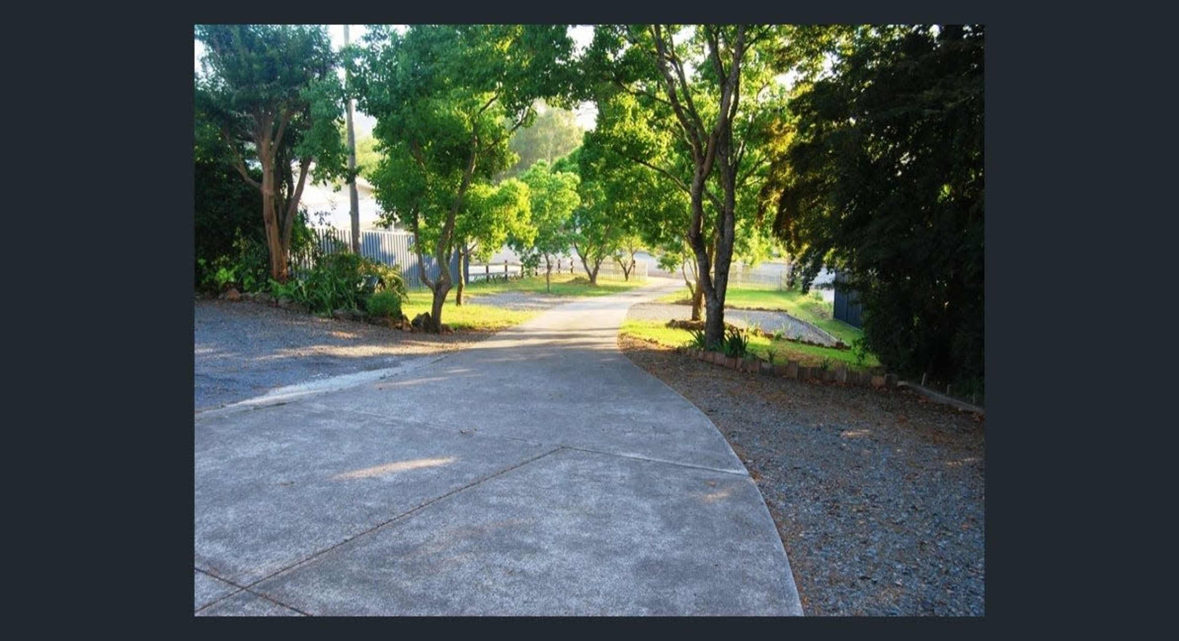 A concrete pathway winds through a tree-lined area, leading into a clear distance.