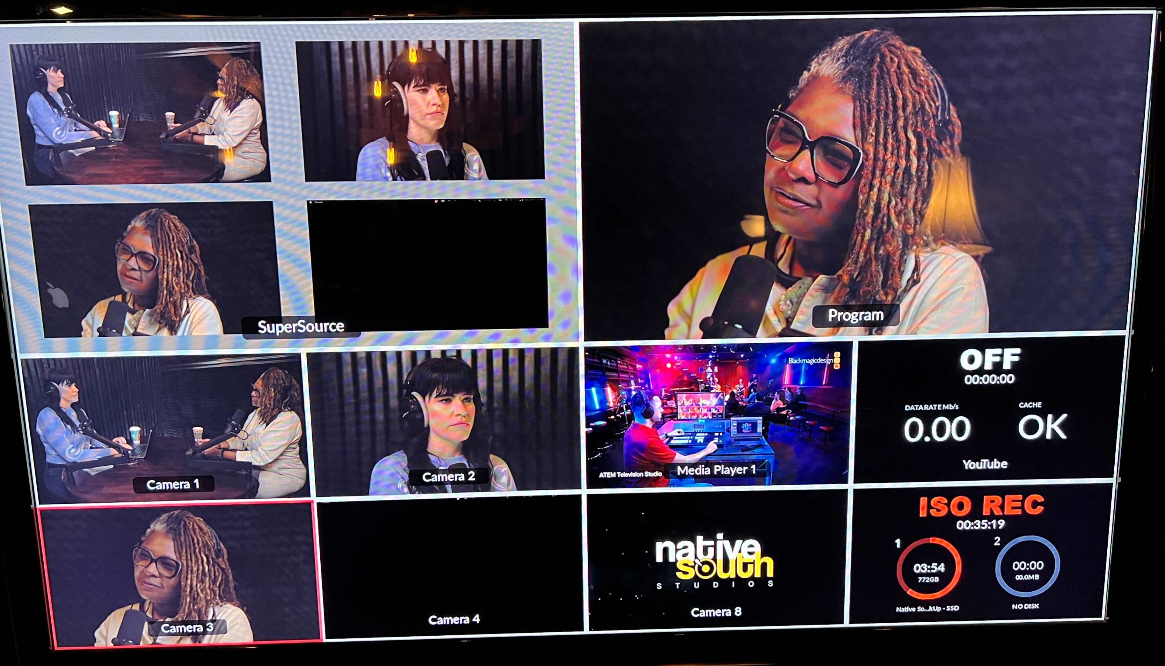 The image shows a television production monitor displaying multiple camera angles of two people engaged in a discussion, with overlays for program information and a control interface.