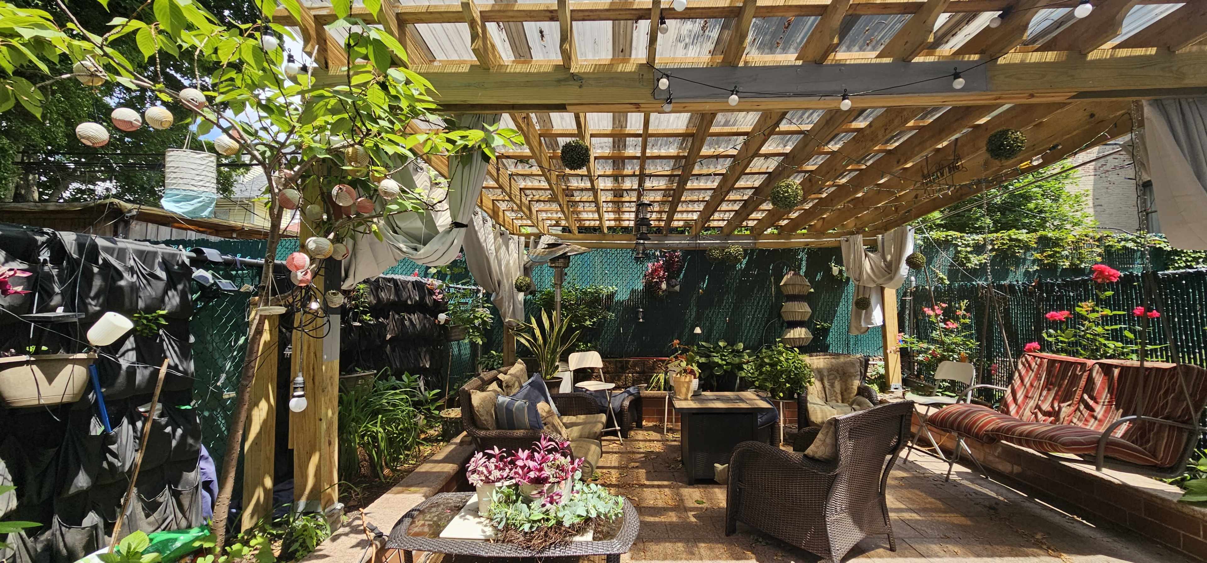 A shaded outdoor patio area adorned with plants, comfortable seating, and decorative string lights.