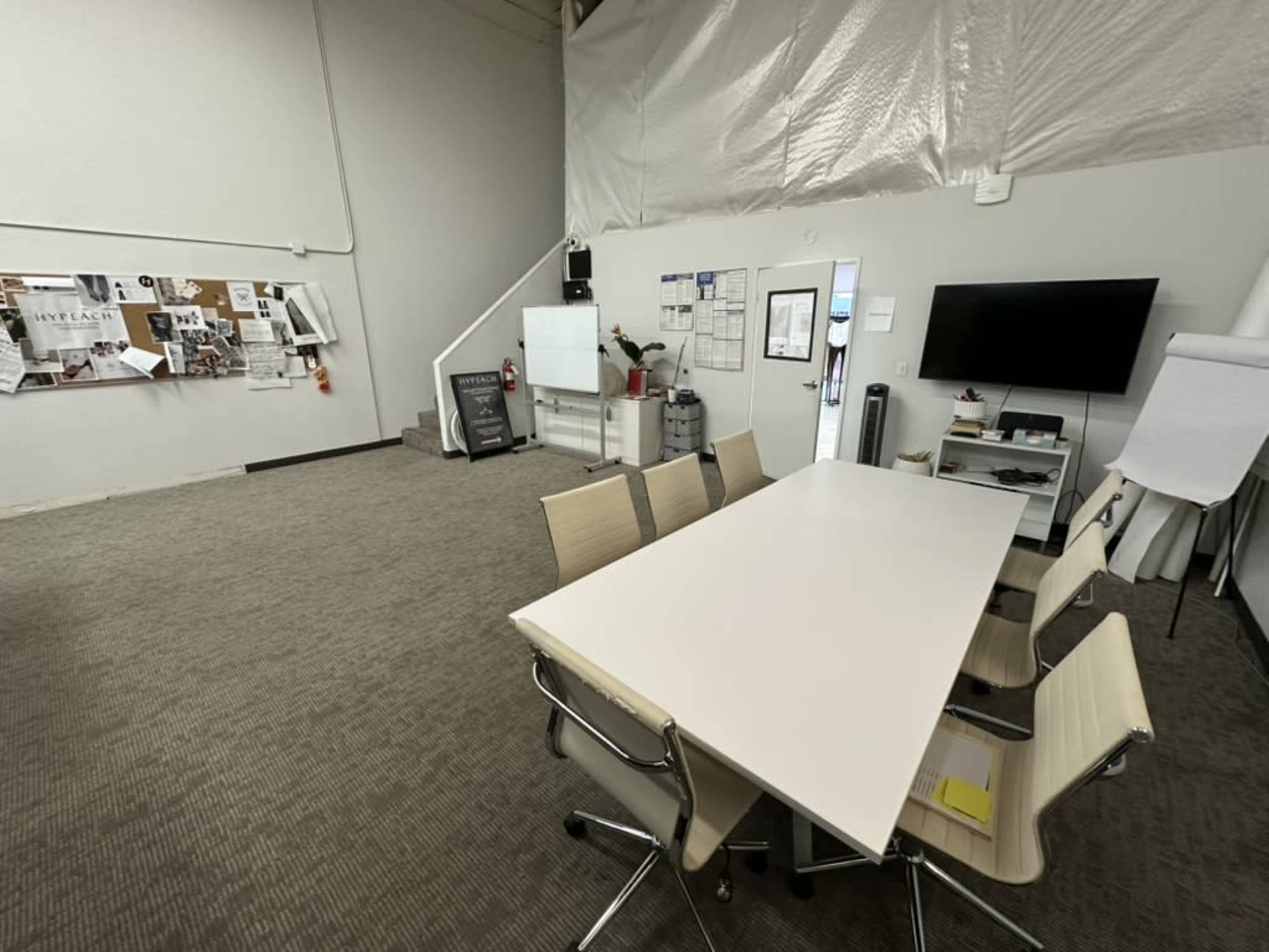 The image shows a conference room with a long white table and several chairs, set in a spacious, minimally decorated environment.