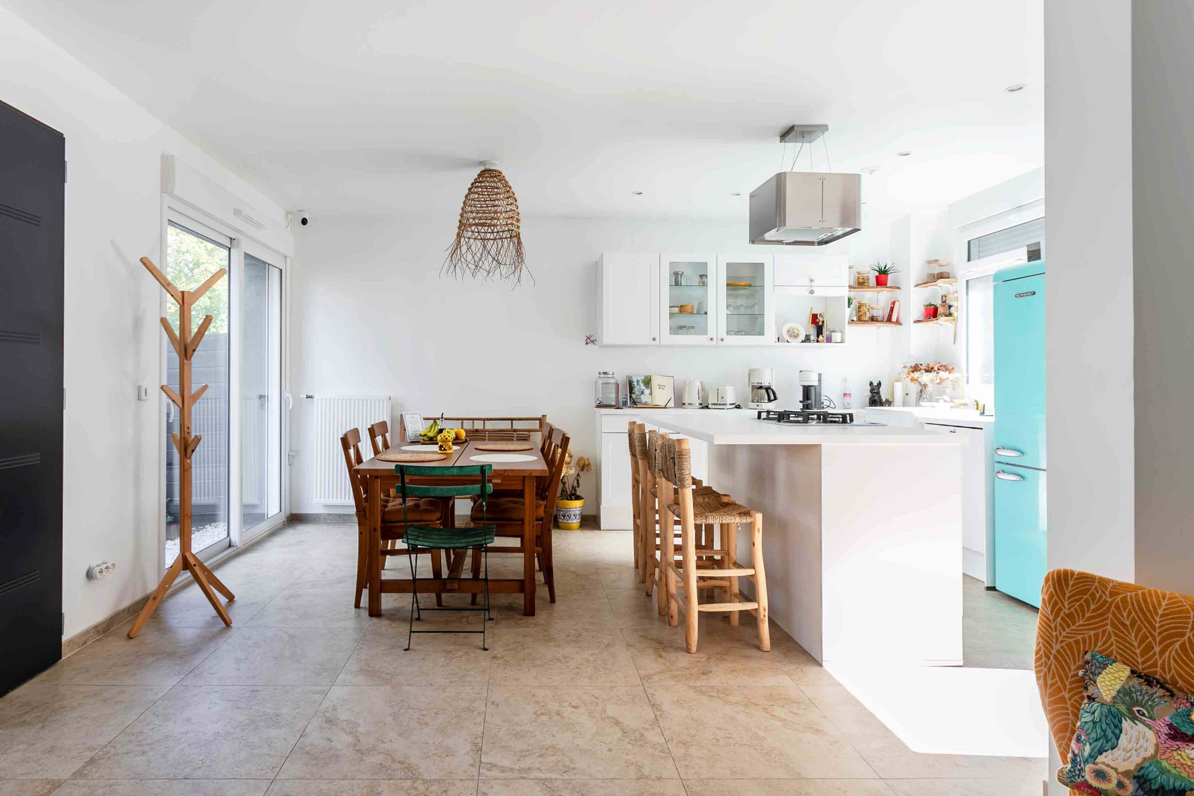 A modern kitchen features a dining table with wooden chairs, light-colored walls, and a bright blue refrigerator.