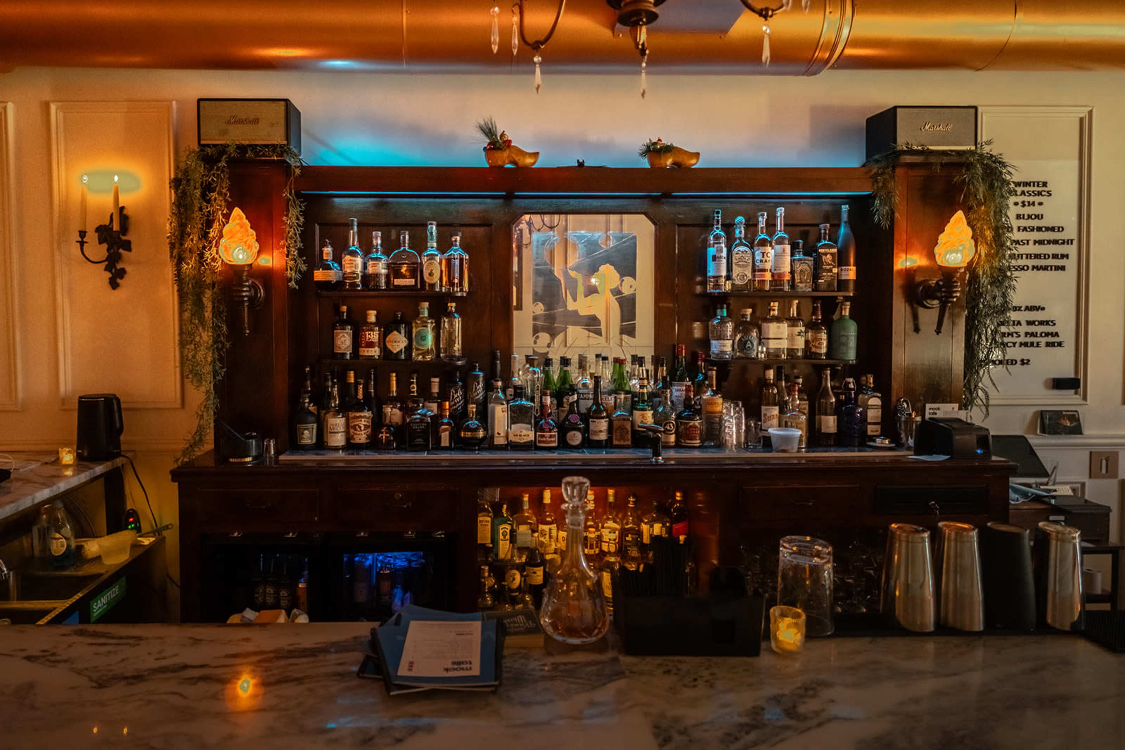 A well-stocked bar with shelves filled with various bottles of alcohol, illuminated by warm lighting.