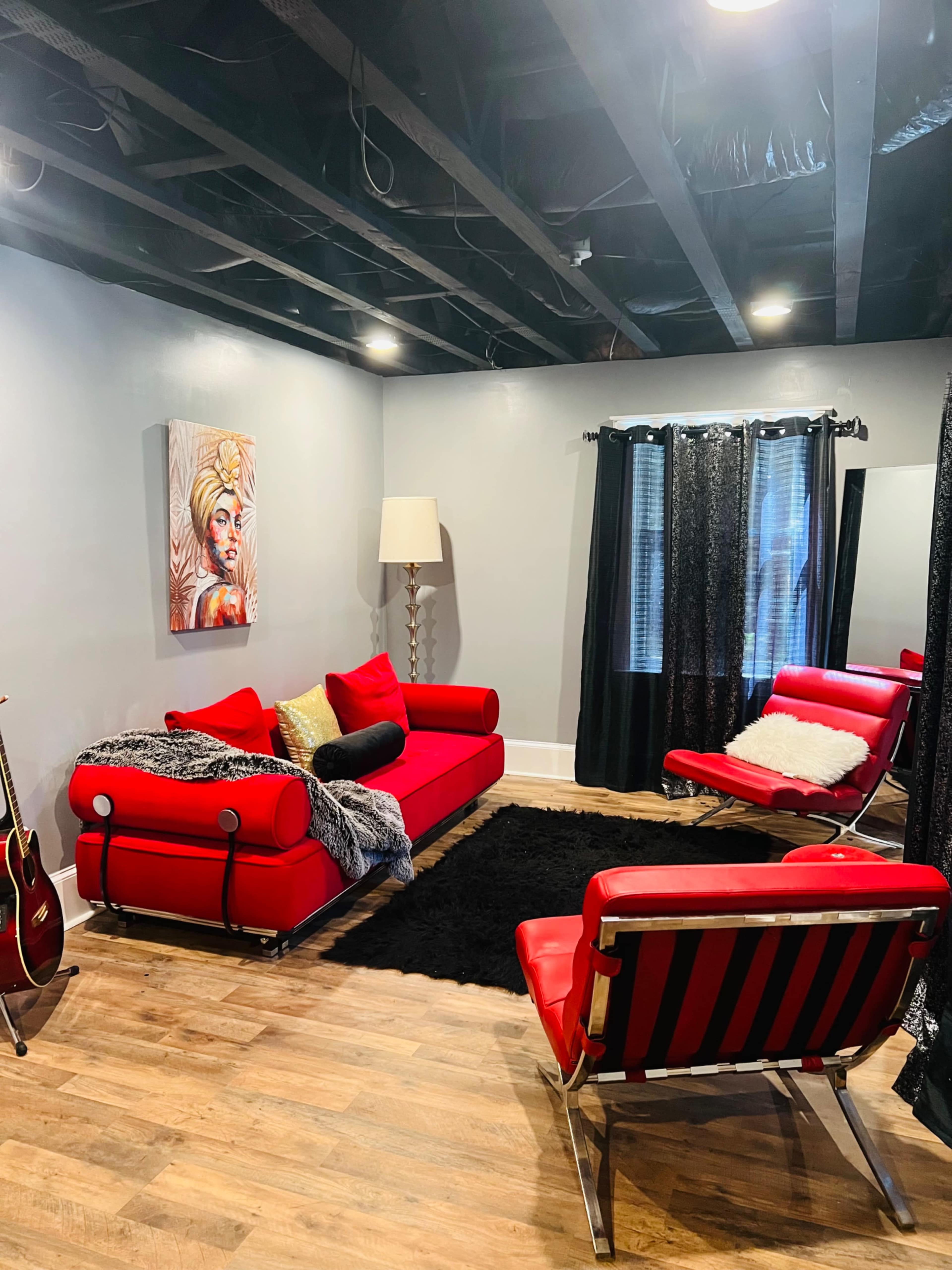 The image shows a modern living room featuring a red sofa, a black shag rug, and a couple of chairs, with artwork and a lamp decor on the walls.