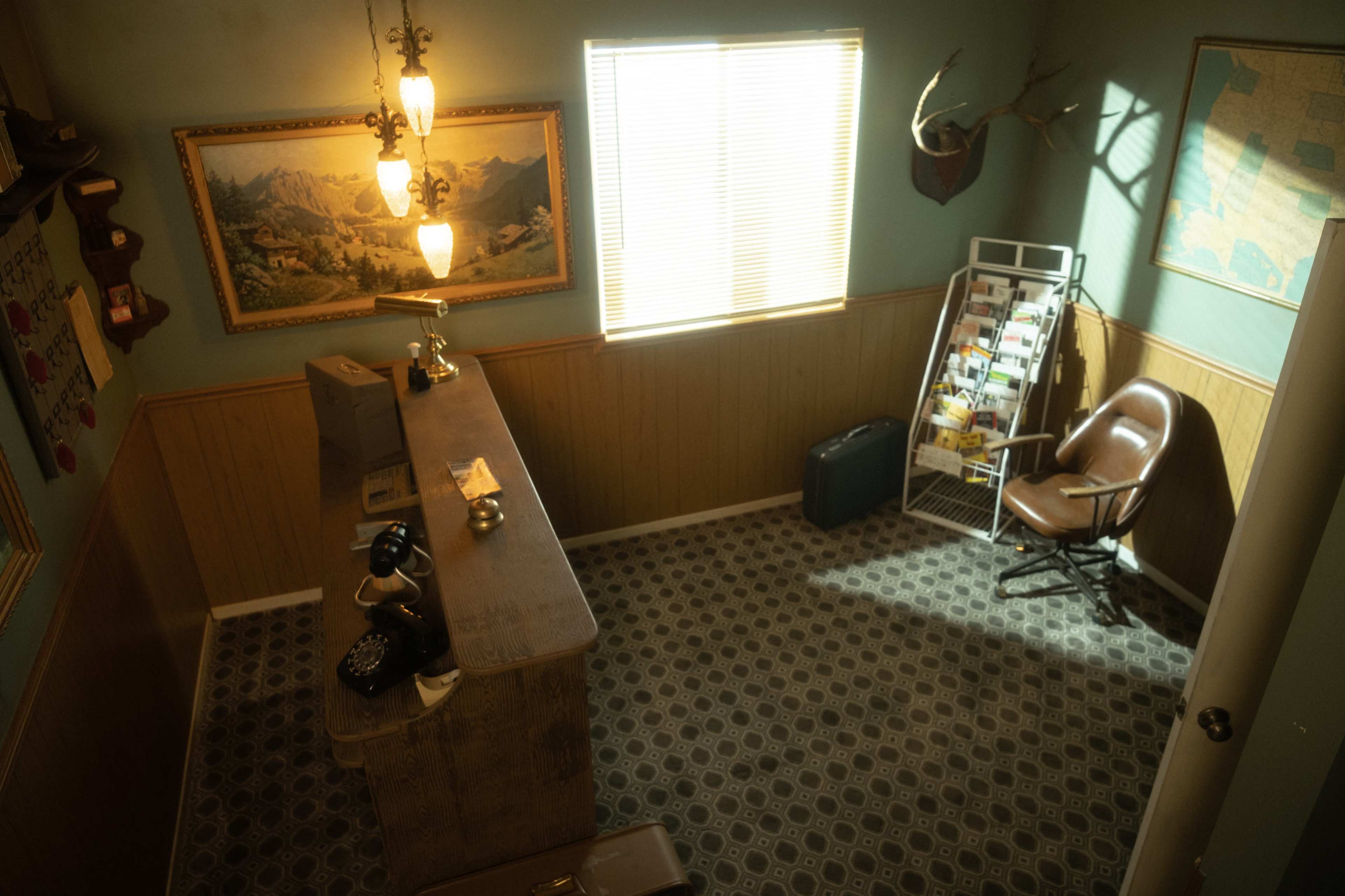 A vintage-style room featuring a wooden reception desk, a chair, a magazine rack, and framed artwork on the walls.