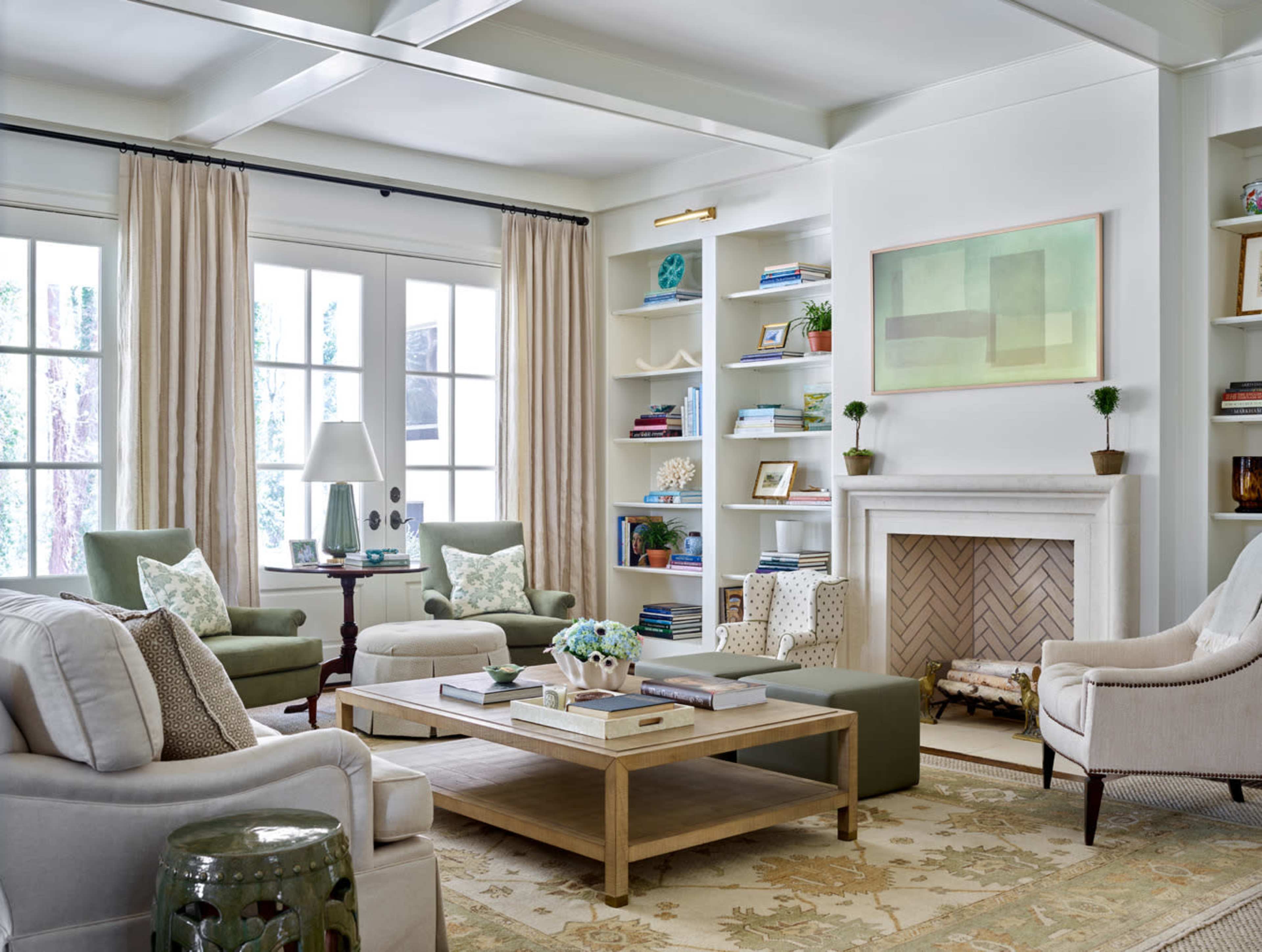 A bright living room featuring a seating area with light-colored sofas, green accent chairs, a wooden coffee table, and built-in bookshelves adorned with decorative items.