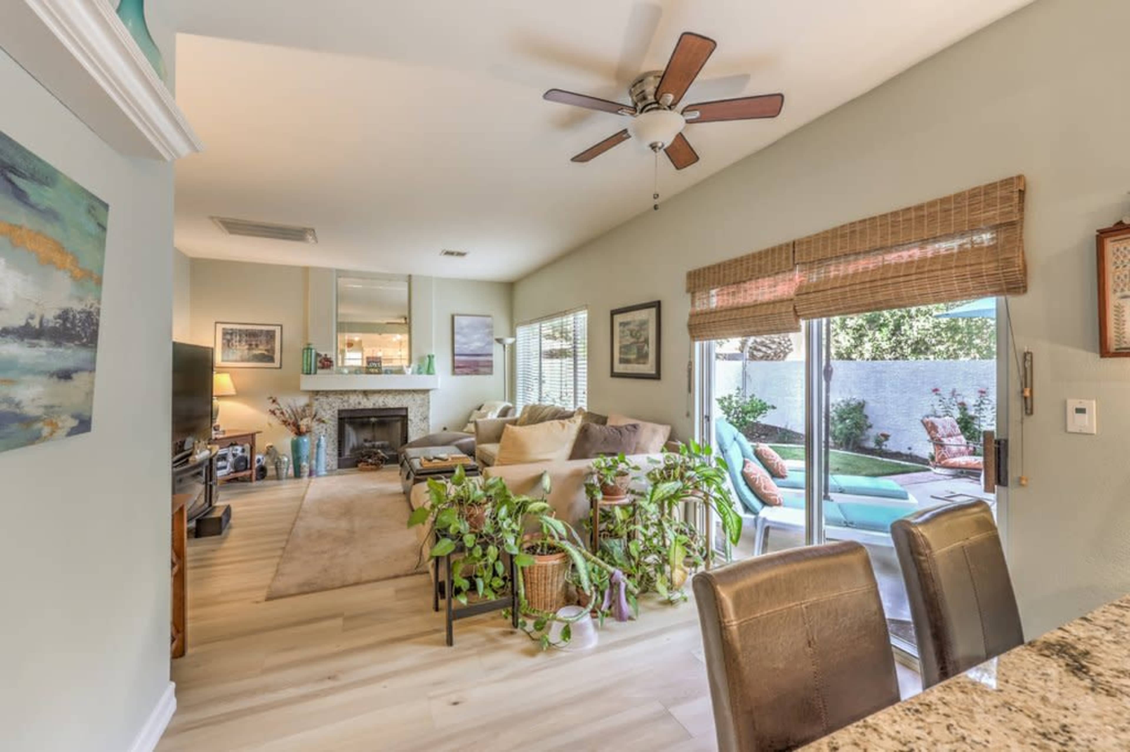 A light-filled living room with a seating area, plants, a fireplace, and sliding glass doors leading to an outdoor space.