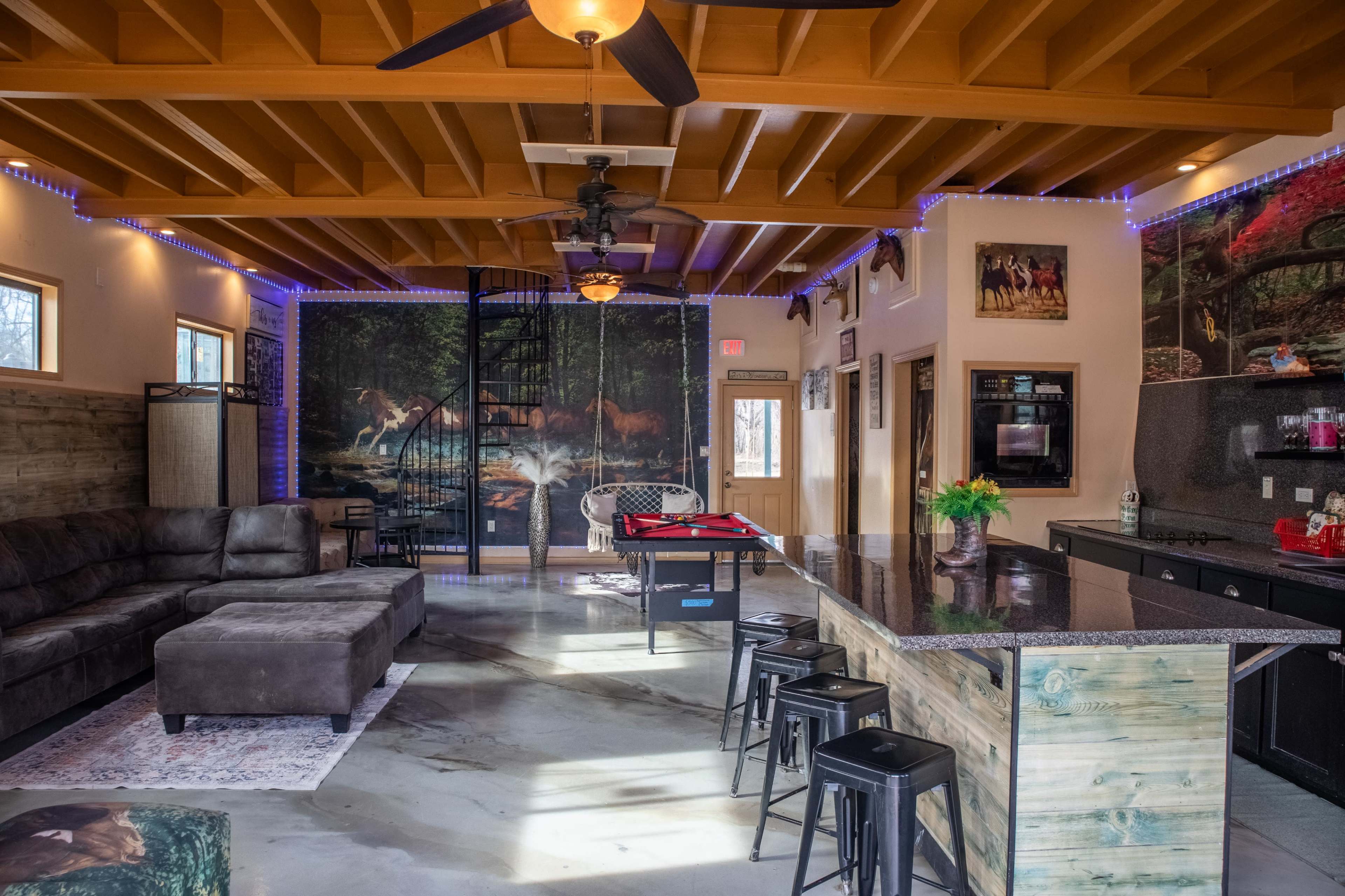 The image shows a spacious living area with a sectional sofa, a pool table, and a kitchen island, featuring decorative wall art and modern lighting.