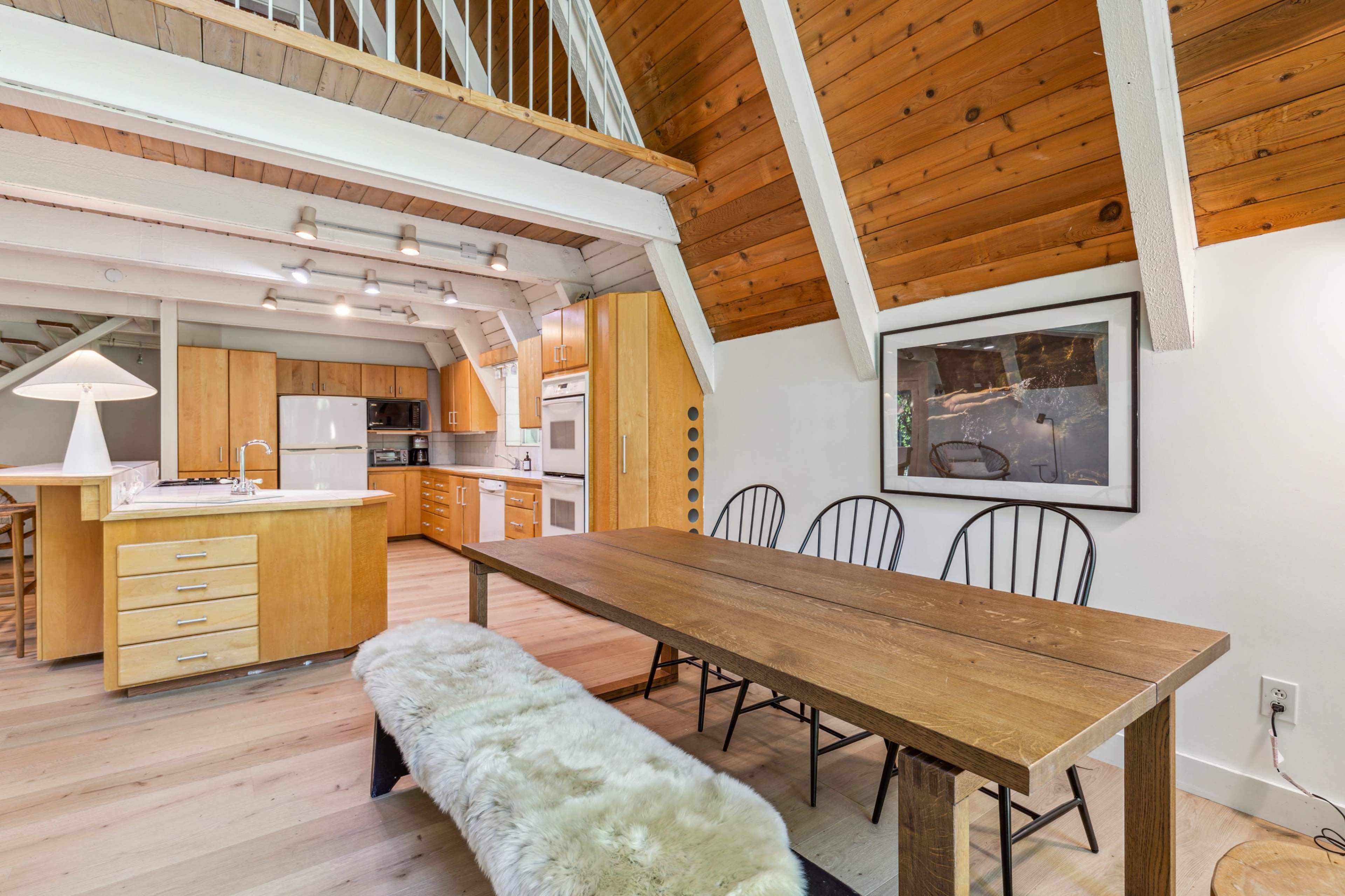 The image shows a modern kitchen and dining area with wooden beams, a large wooden table, and a bench.