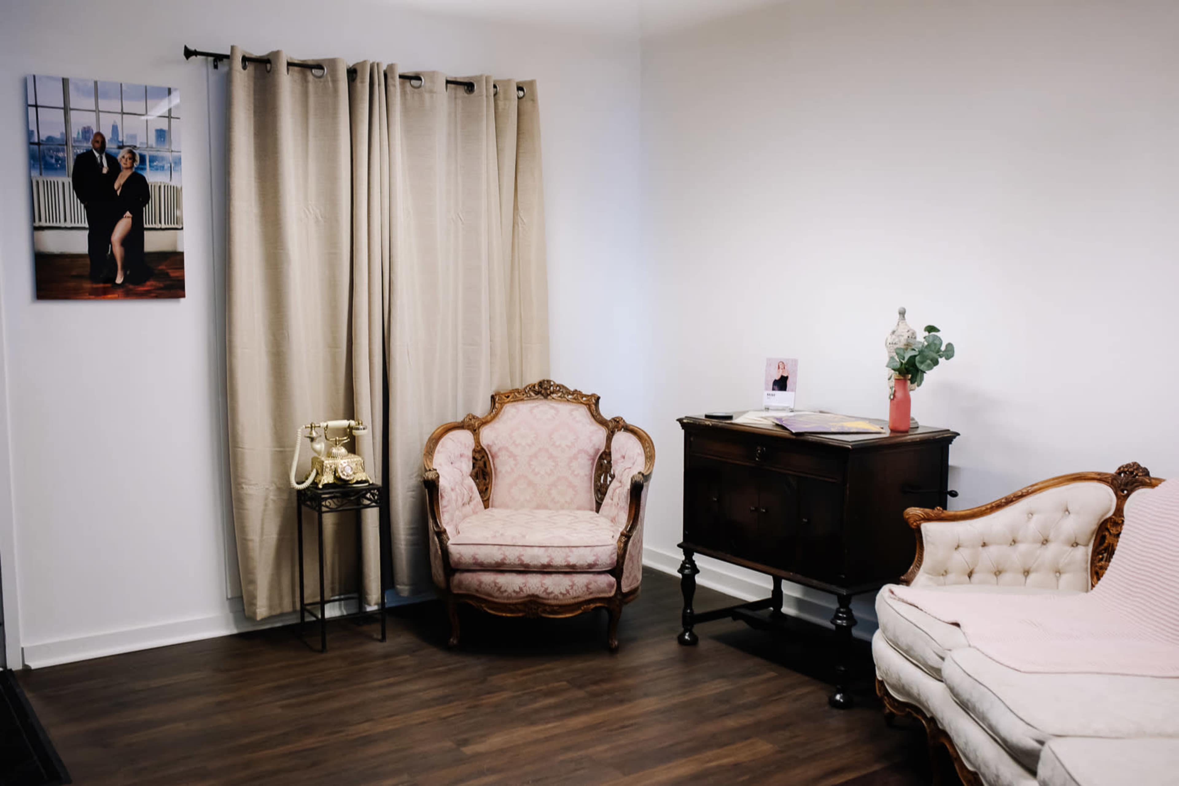 A cozy living room with a vintage telephone, a floral armchair, a wooden cabinet, and beige curtains covering a window.