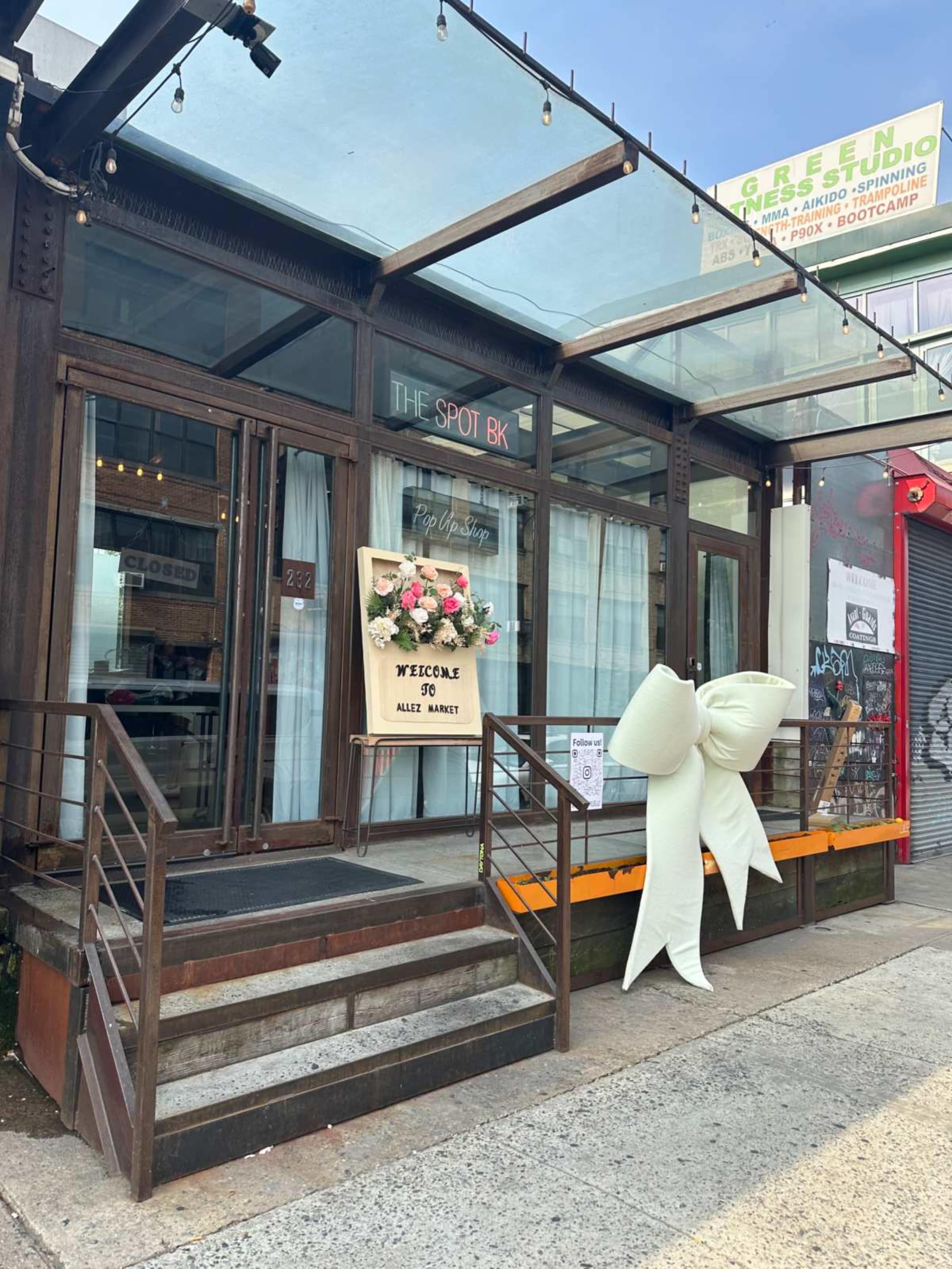 The storefront features a modern design with large windows, a decorative sign reading "The Spot BK," and a floral arrangement on display.