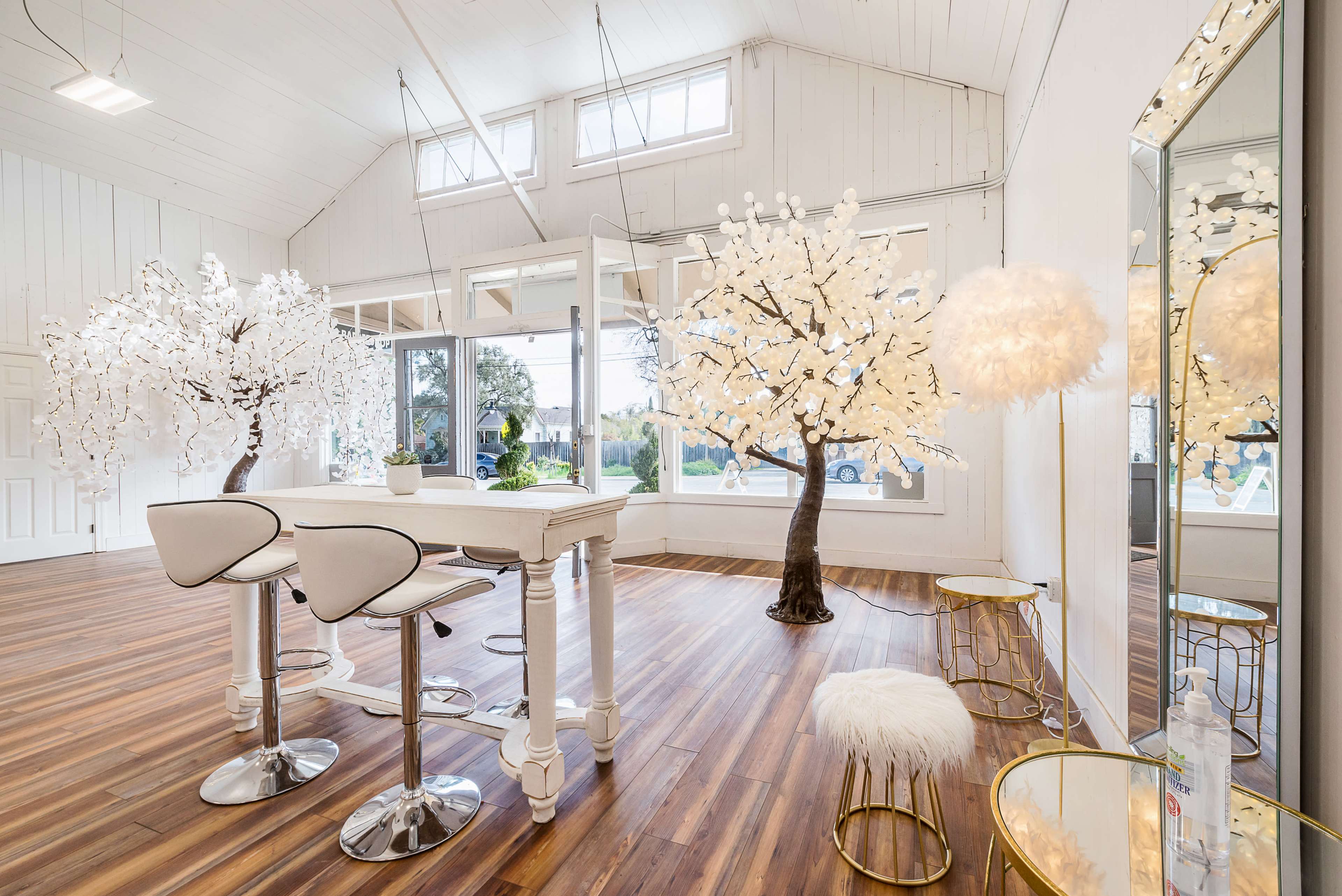 A bright room with two decorative trees adorned with white lights, a white bar table, and stylish seating.