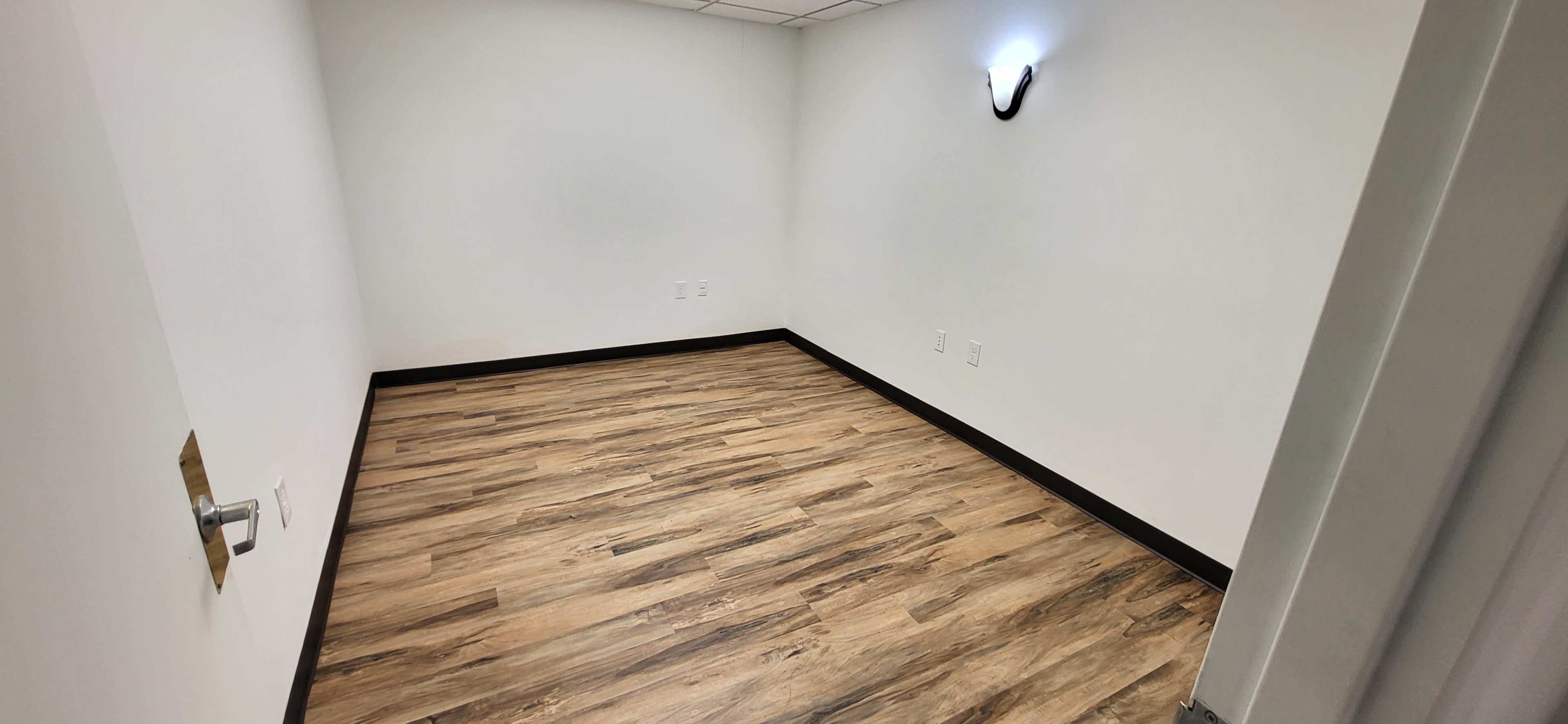 An empty room with wooden flooring and a single wall-mounted light fixture.