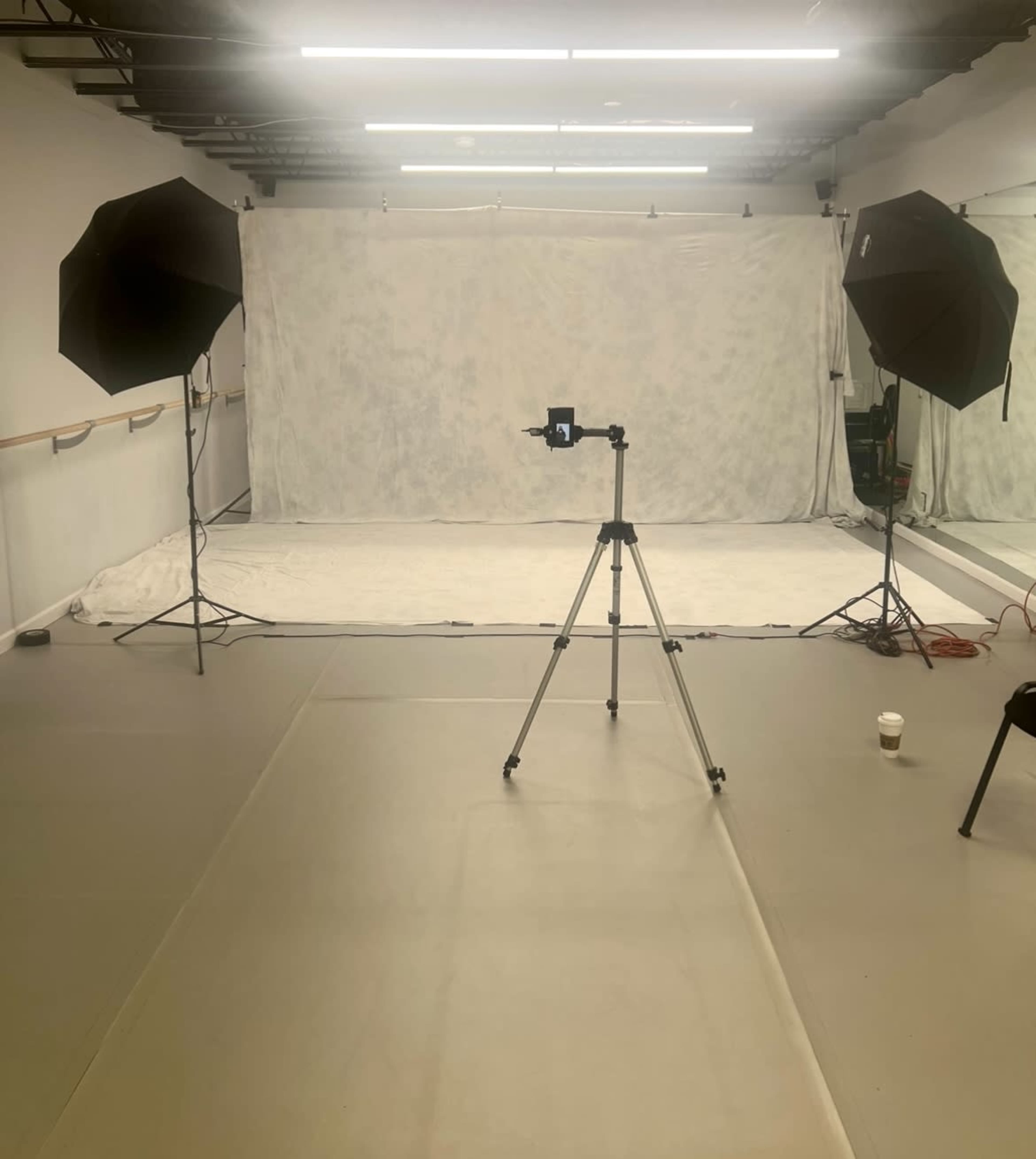 The image shows a photography studio set up with two softbox lights, a camera on a tripod, and a light-colored backdrop.