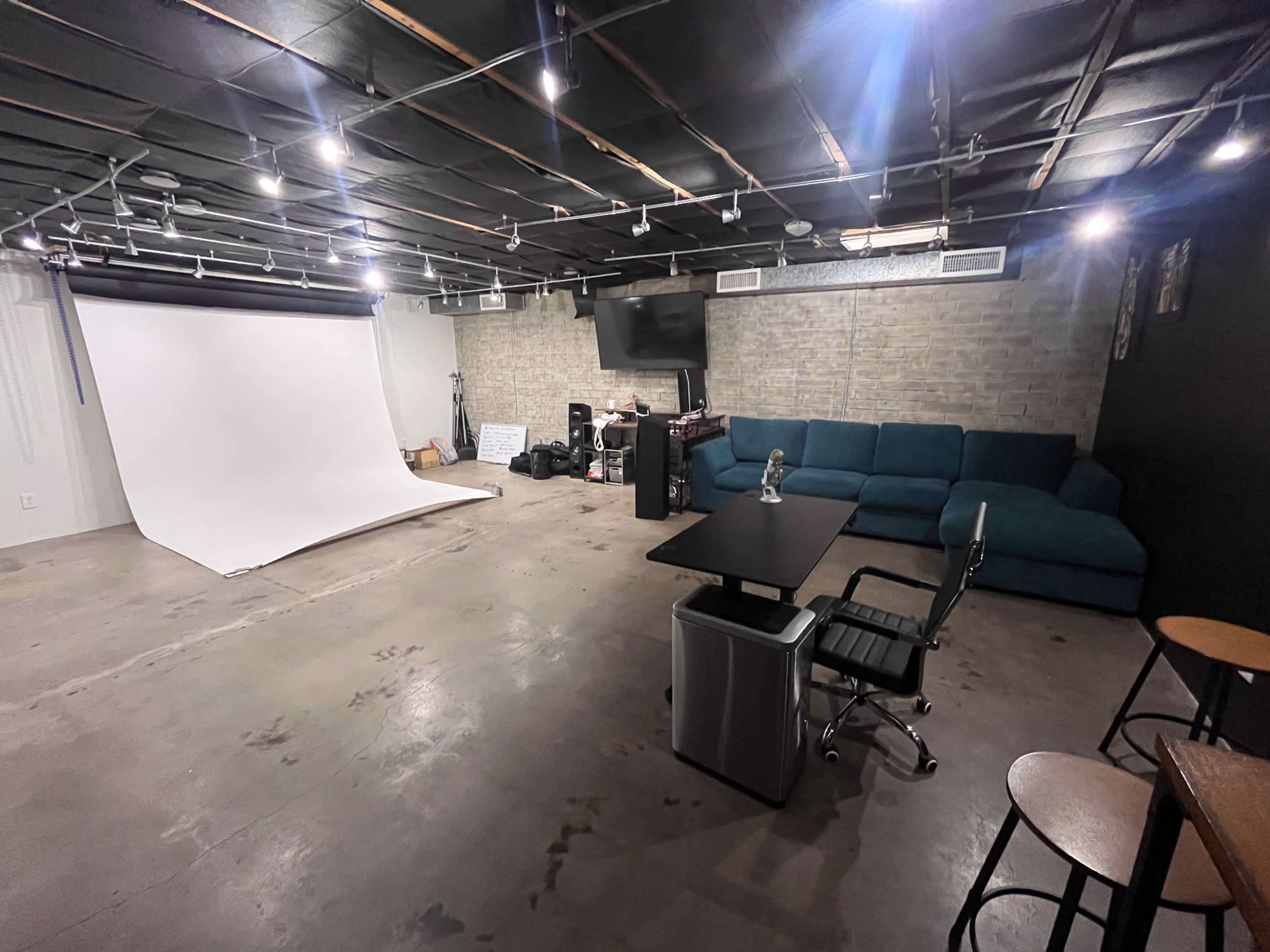 A spacious studio with a white backdrop setup, seating area, and equipment arranged along the walls.