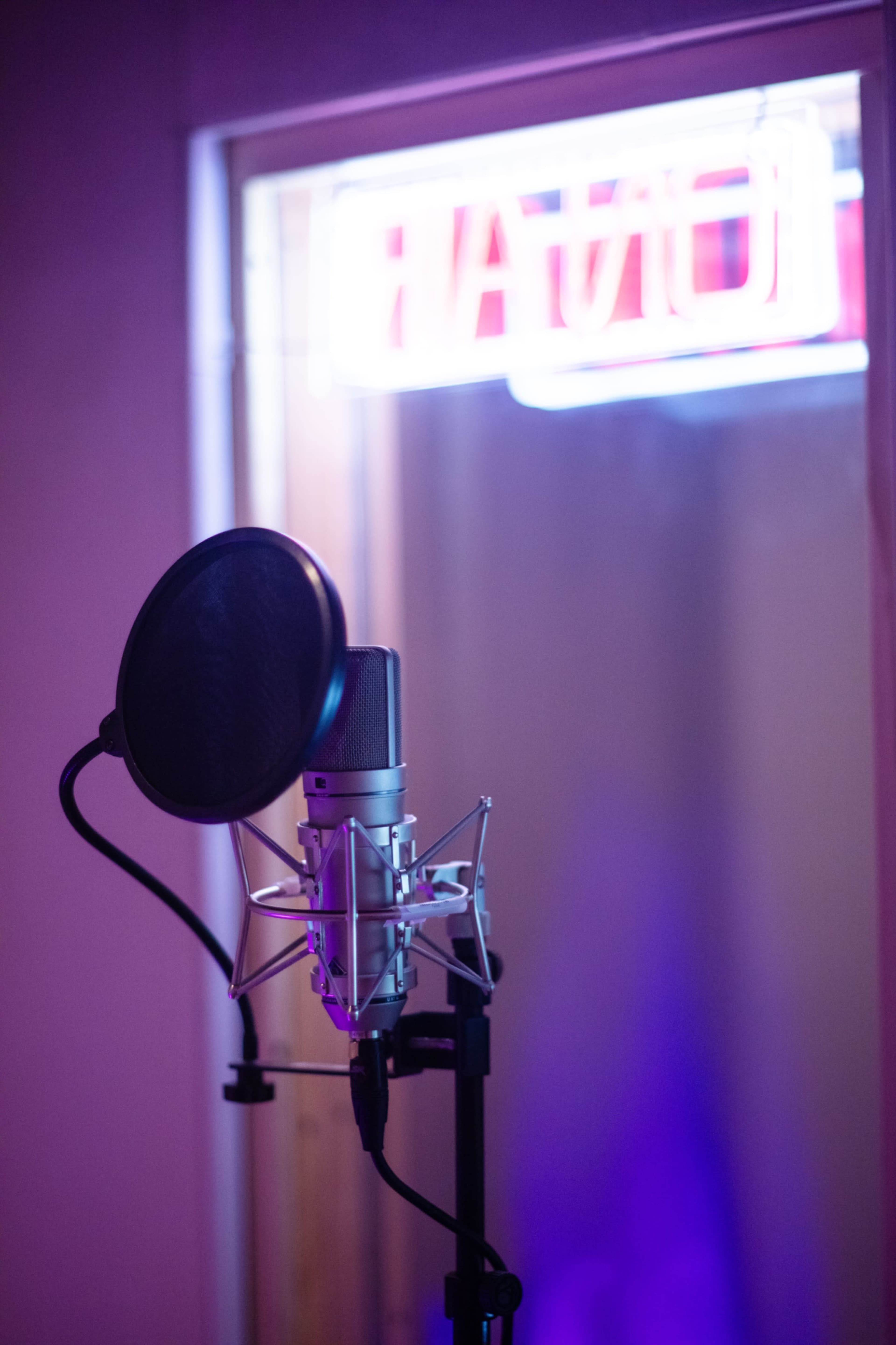 A microphone stands on a stand in front of a glass booth illuminated by a neon sign.