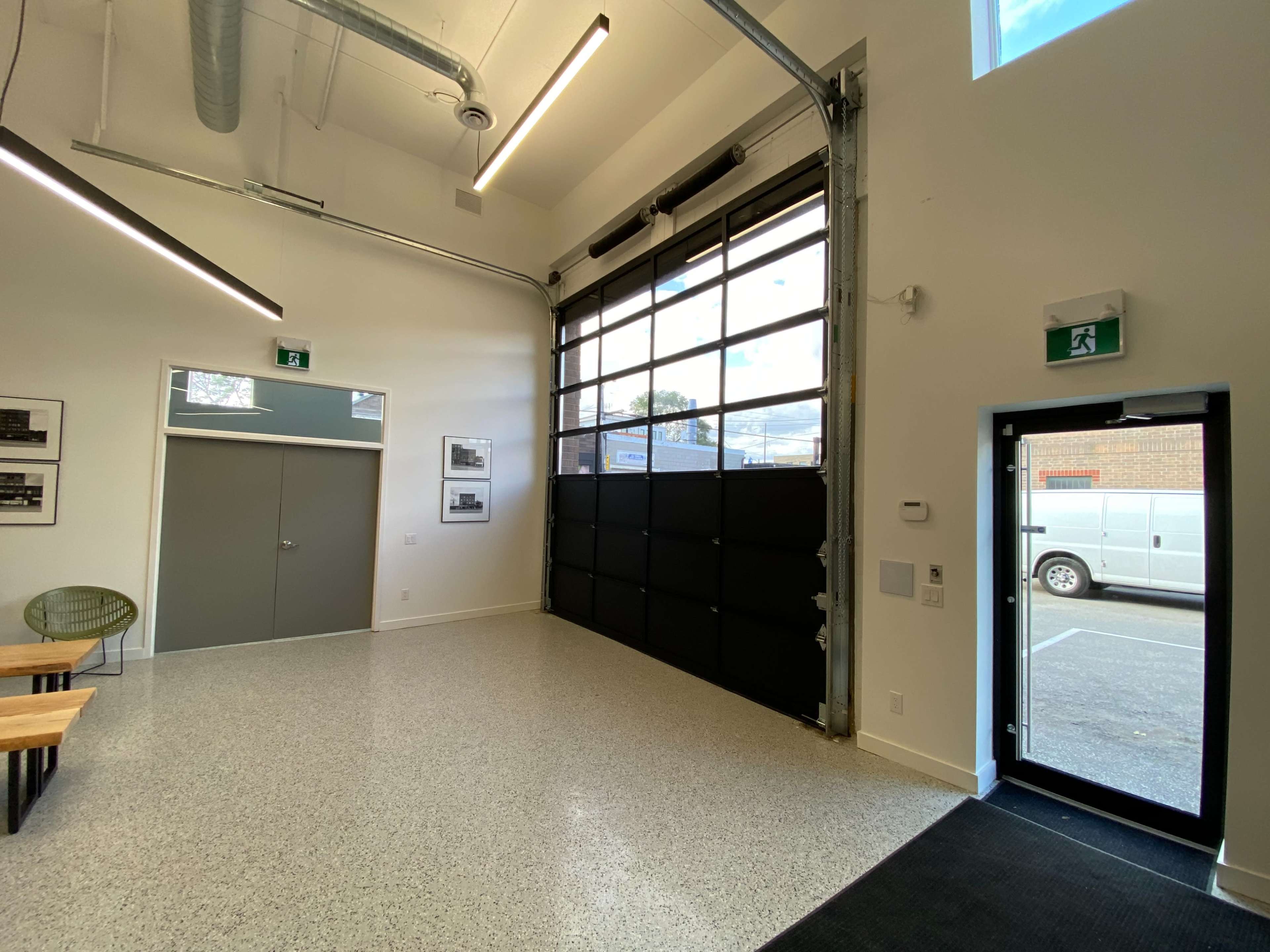 An indoor space with a large glass garage door, two doors on the left side, a small table with wooden top and metal legs, and a view of a parked vehicle outside.