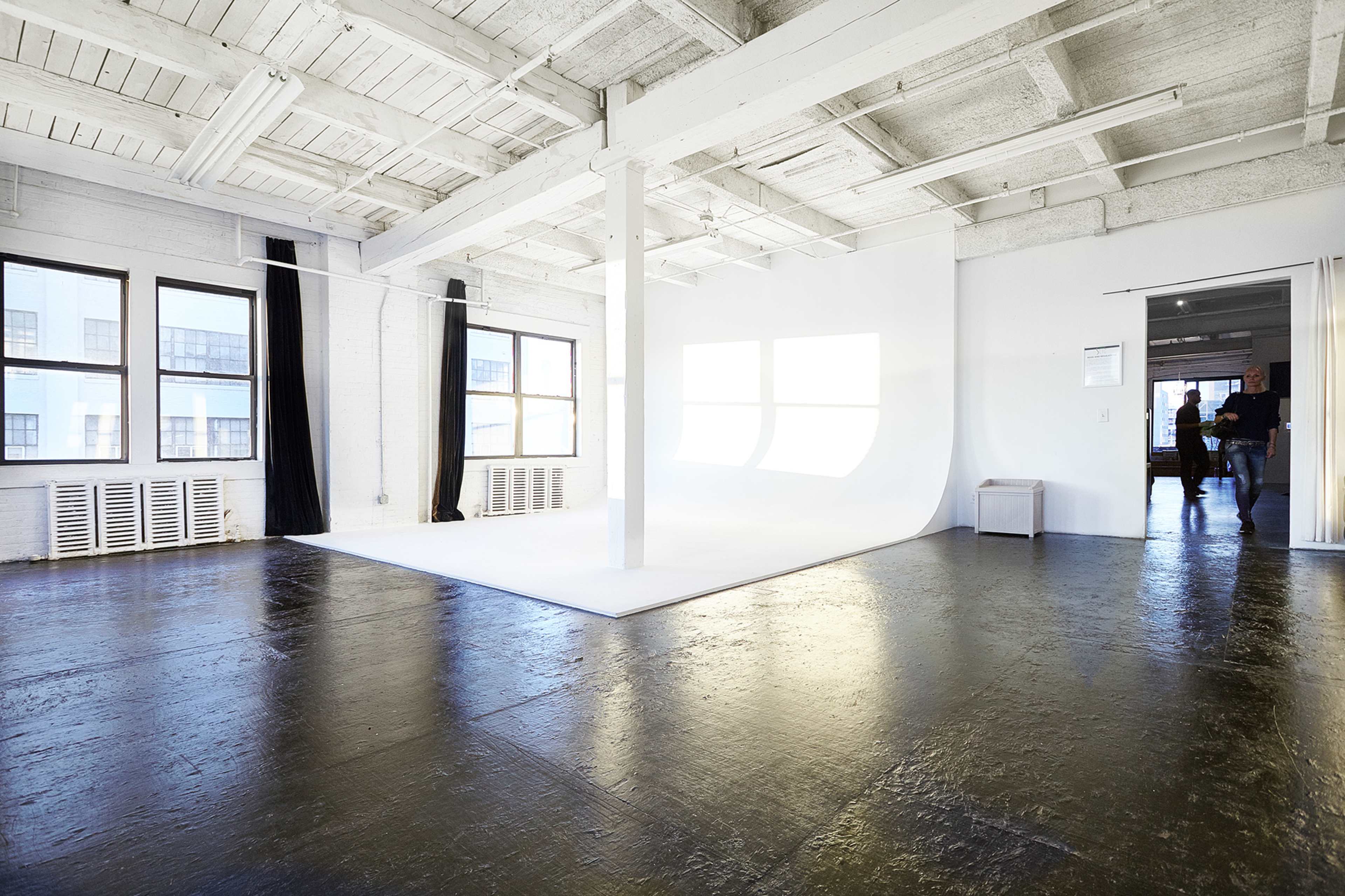 A spacious studio with white walls, large windows, and a seamless backdrop.