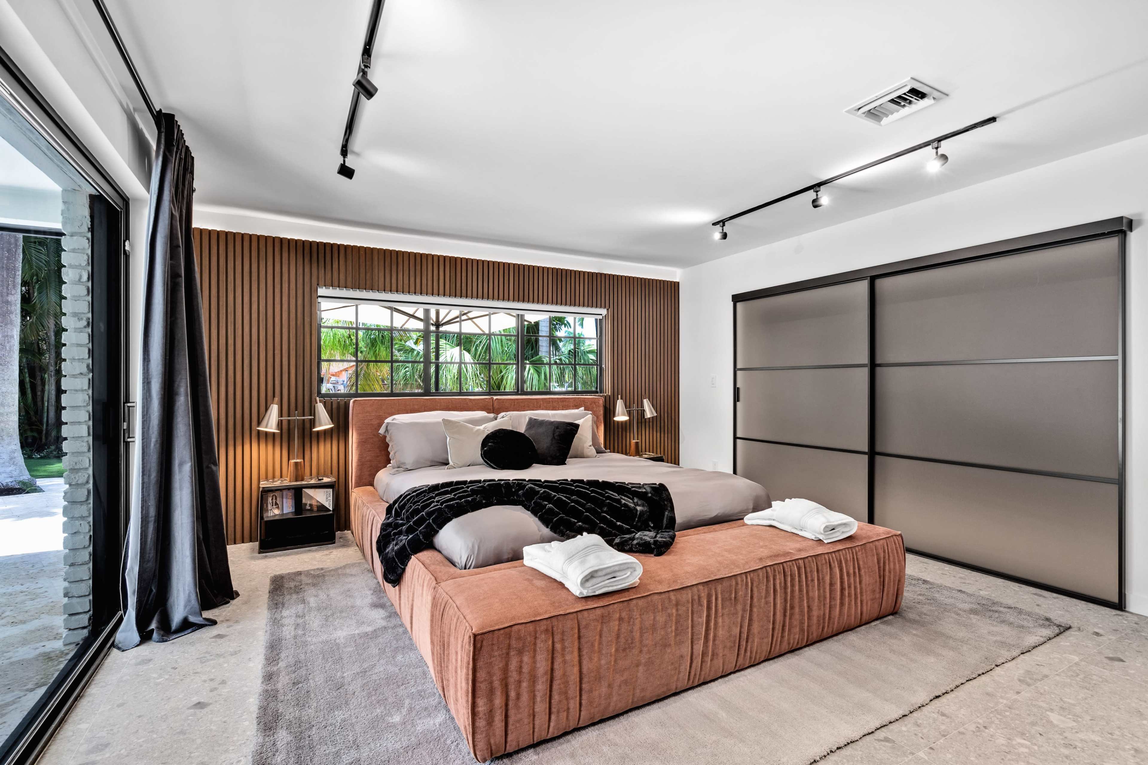 A modern bedroom with a large bed, wooden accent wall, and sliding glass doors opening to an outdoor space.