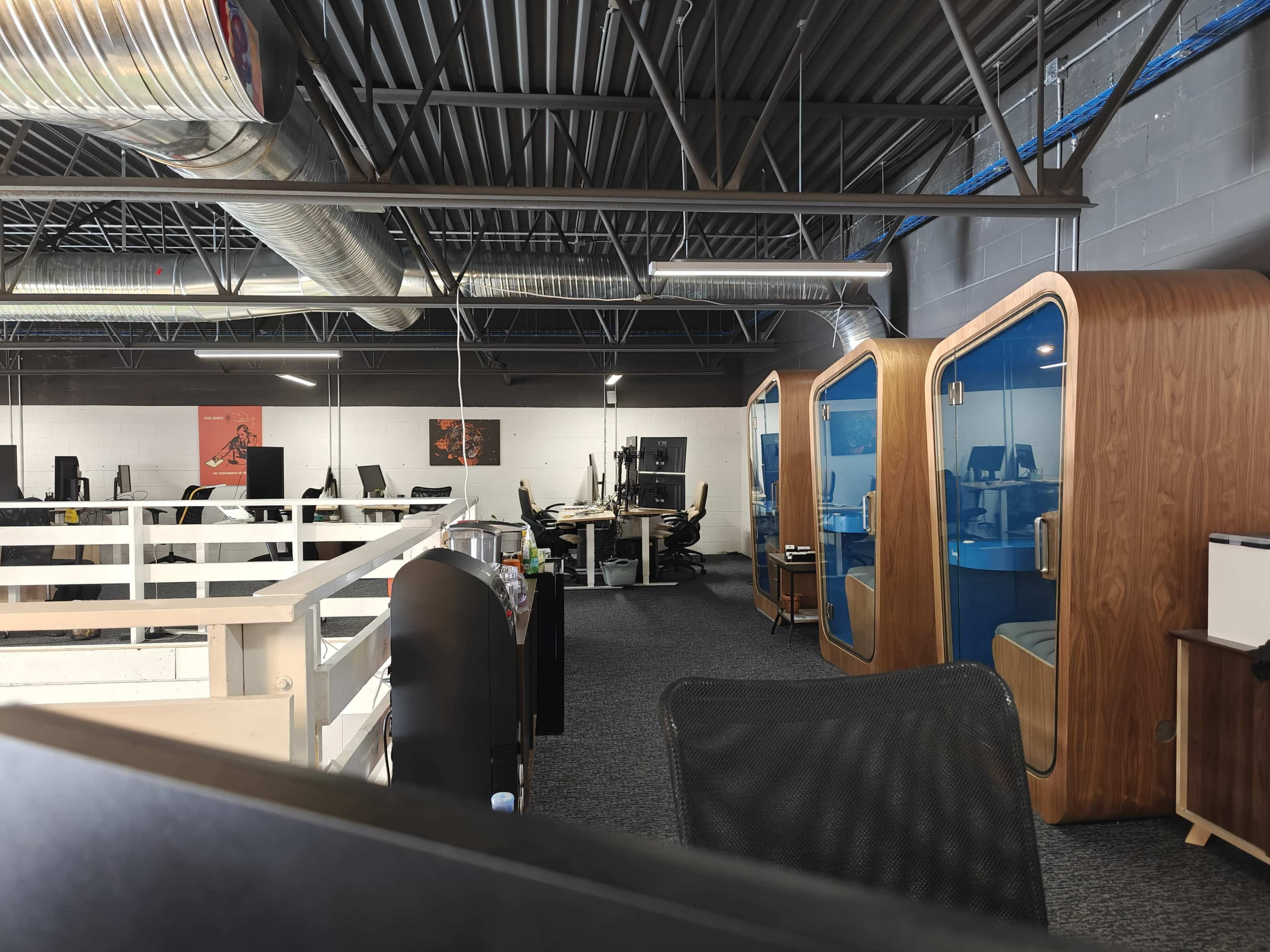 An open office space with wooden privacy pods, work desks, and large windows.