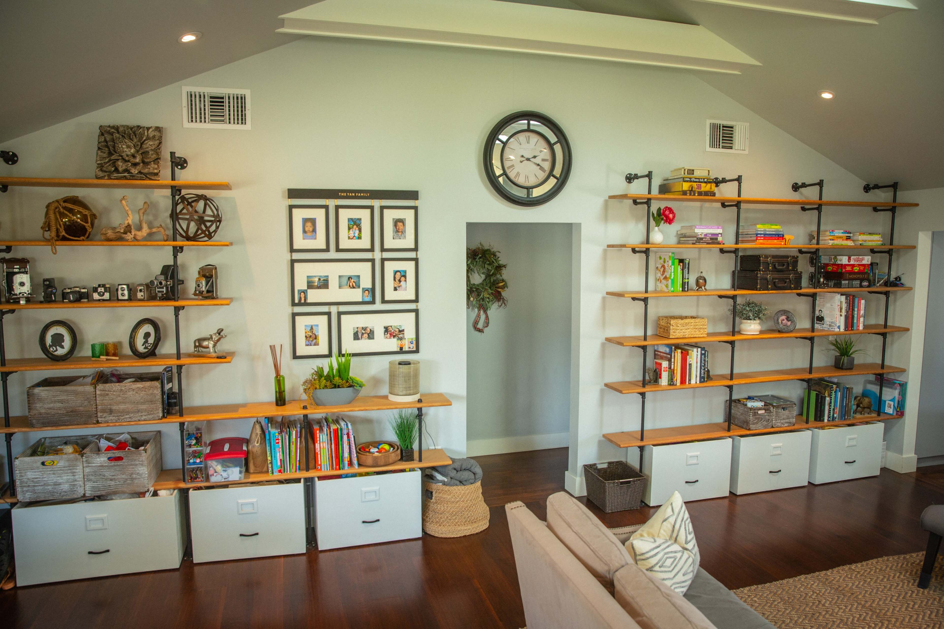 A well-organized room featuring open shelving units filled with books, decorative items, and storage bins, alongside a large clock mounted on the wall.