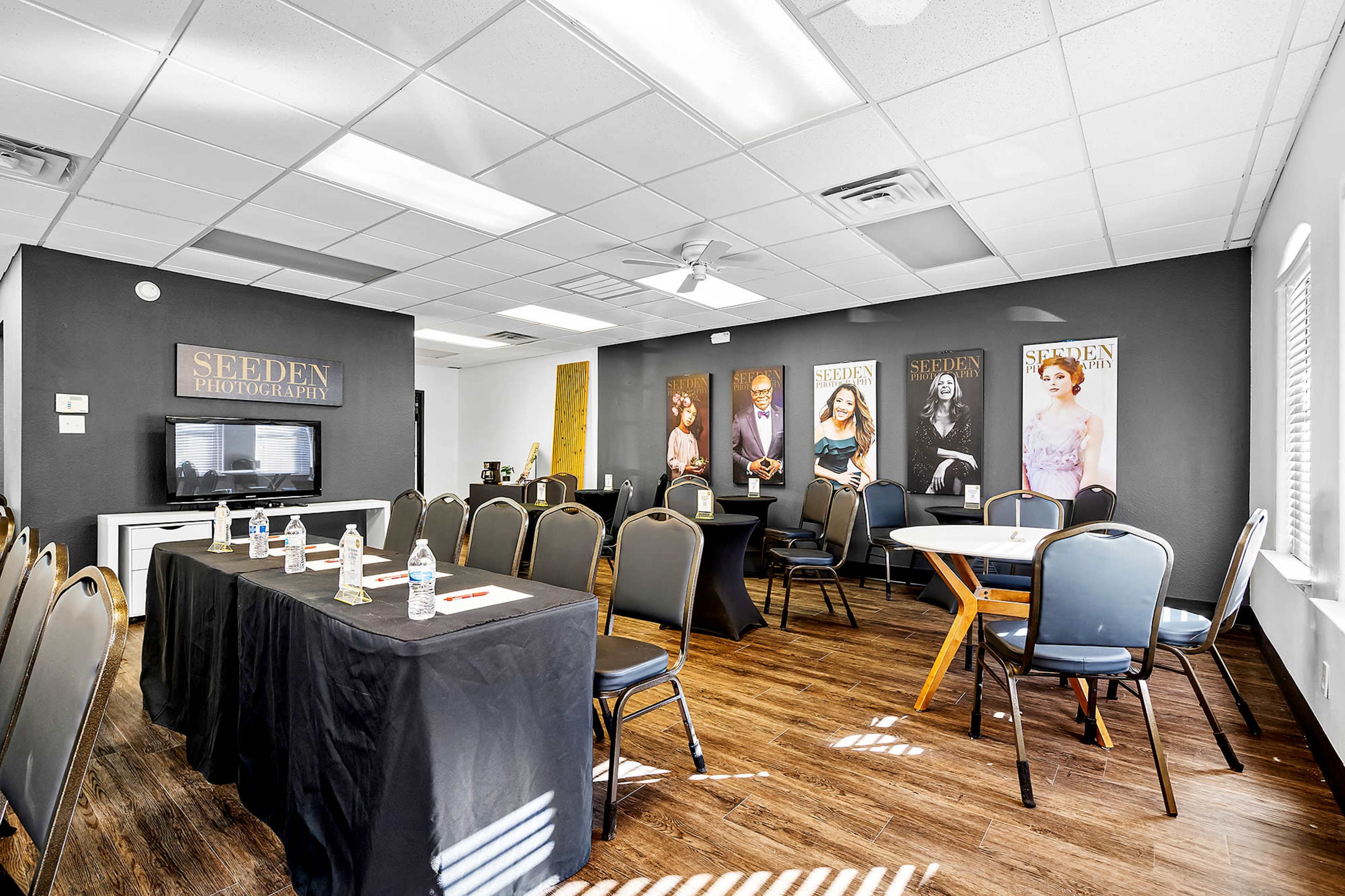 A spacious photography studio with rows of chairs and tables set up for a meeting or event, featuring a television and photographs on the walls.