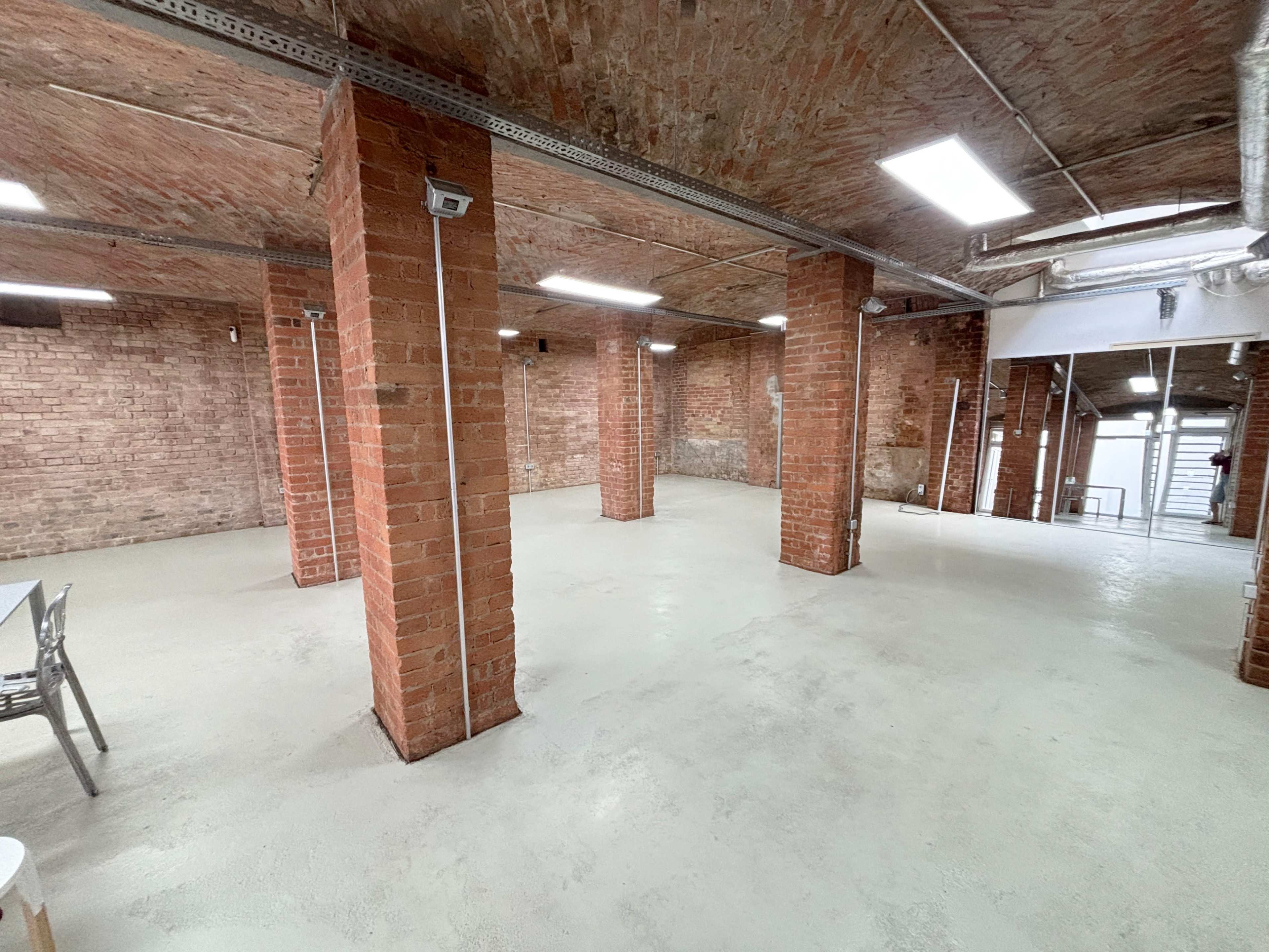 The image shows a spacious, empty industrial warehouse with exposed brick columns and a concrete floor.
