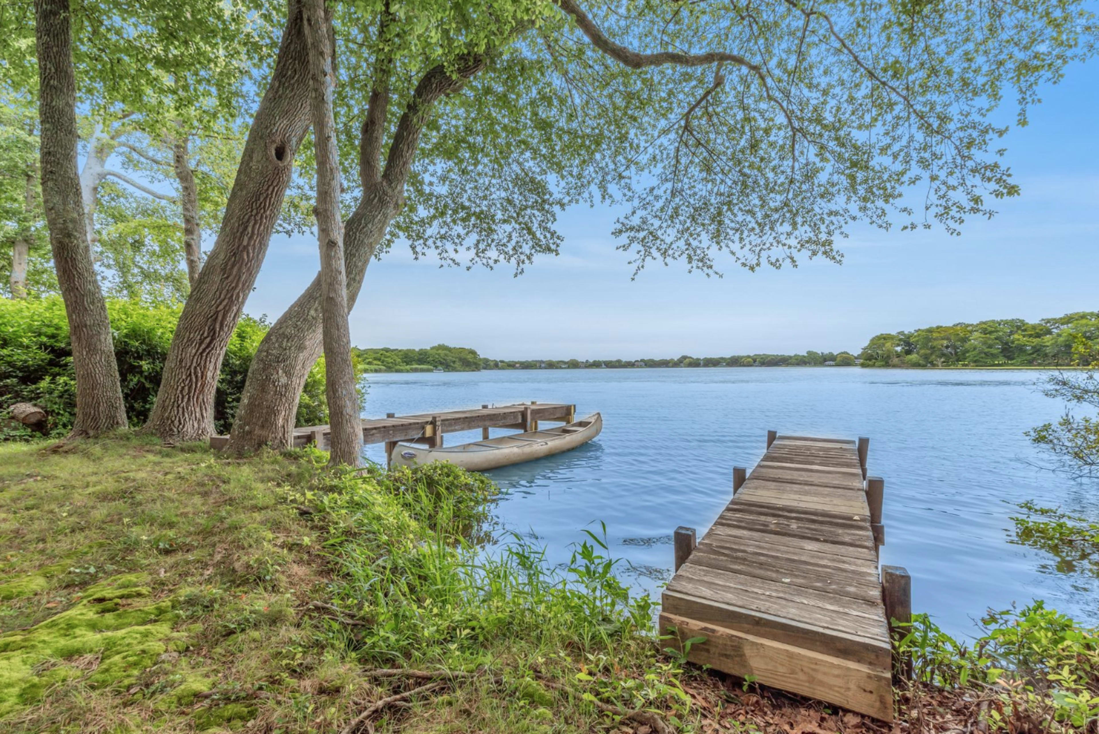 A wooden dock extends into a calm lake surrounded by trees and greenery.