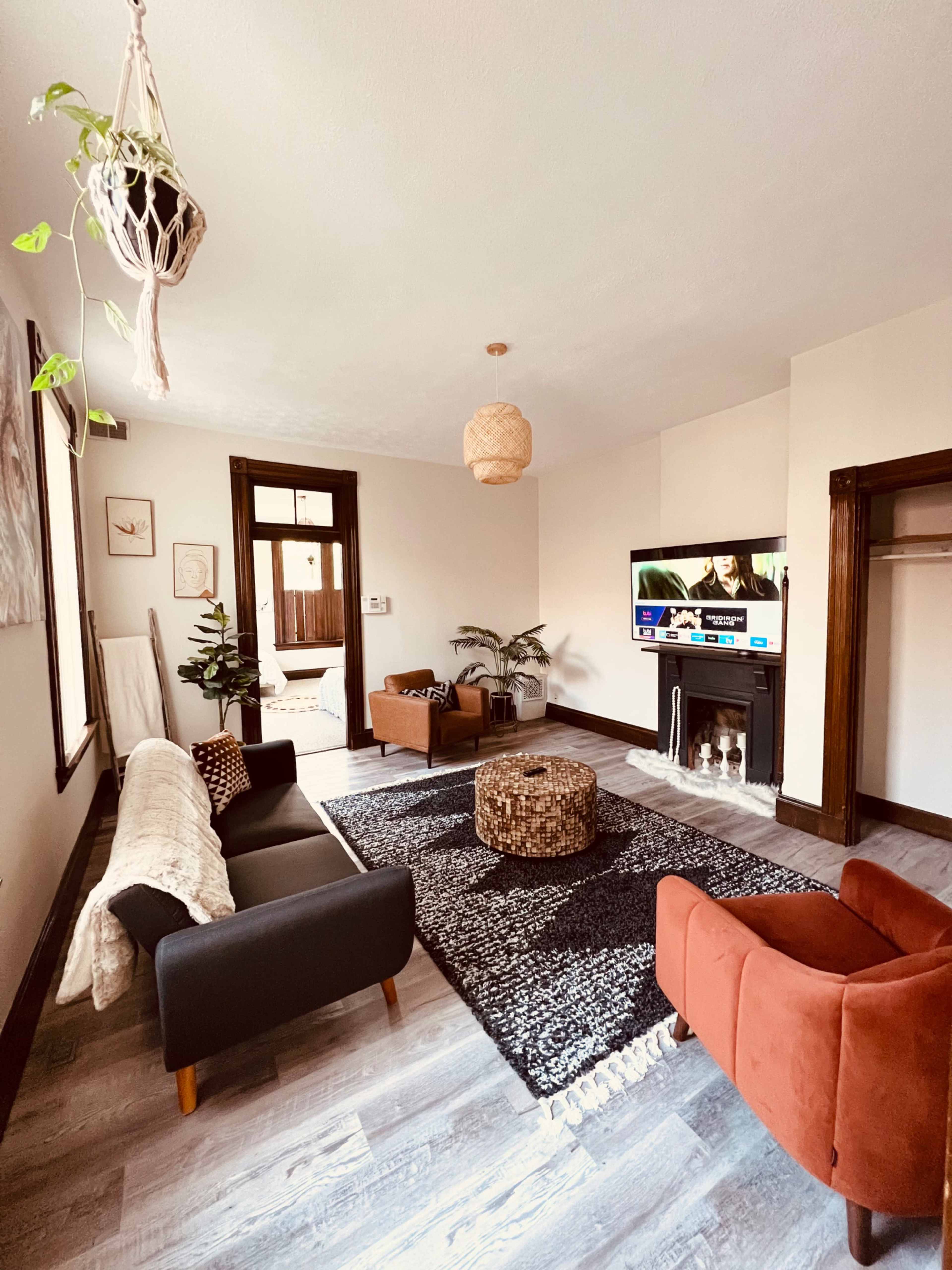 A living room with two armchairs, a sofa, a coffee table, a television, and decorative plants on wooden floors.