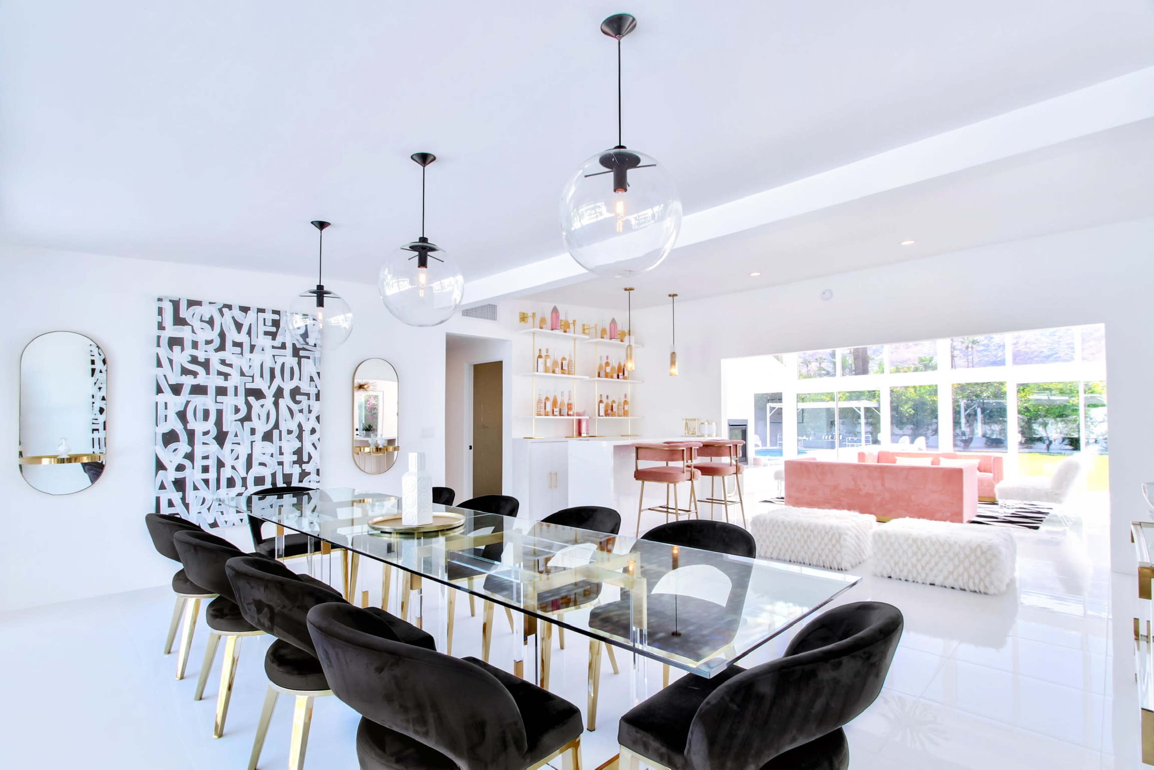 A modern dining area features a glass table surrounded by black chairs, with an artistic wall and a well-lit bar in the background.