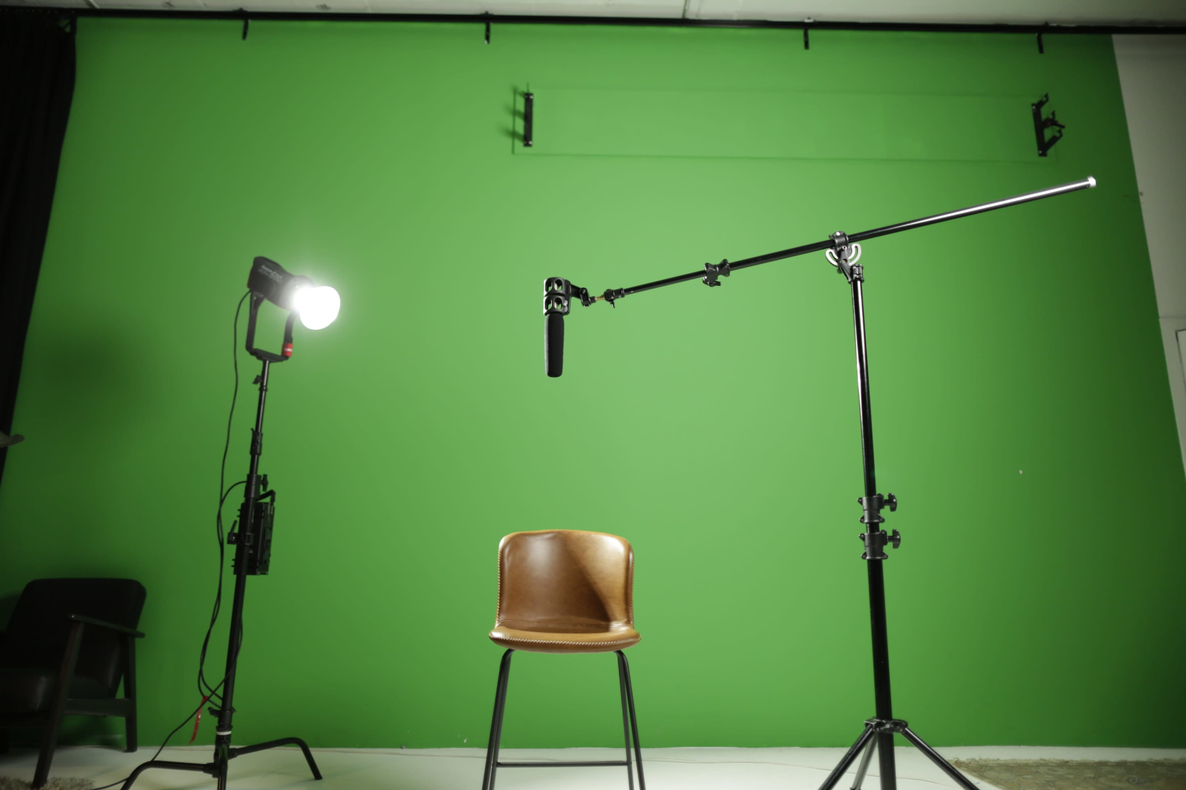A brown chair is positioned in front of a green backdrop, with a spotlight and a microphone setup on either side.
