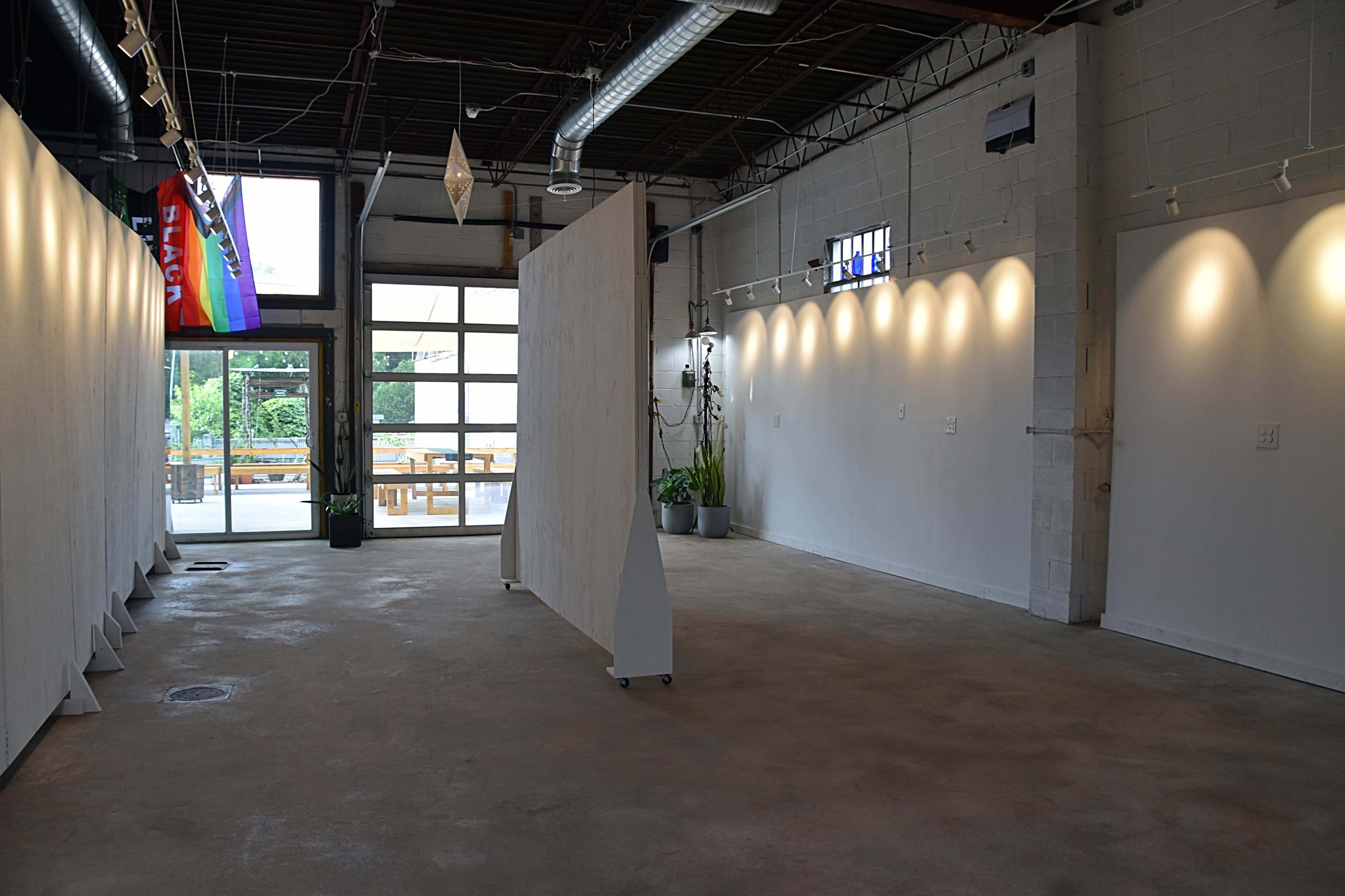 An empty art gallery with white walls, a concrete floor, and large windows allowing natural light to enter.