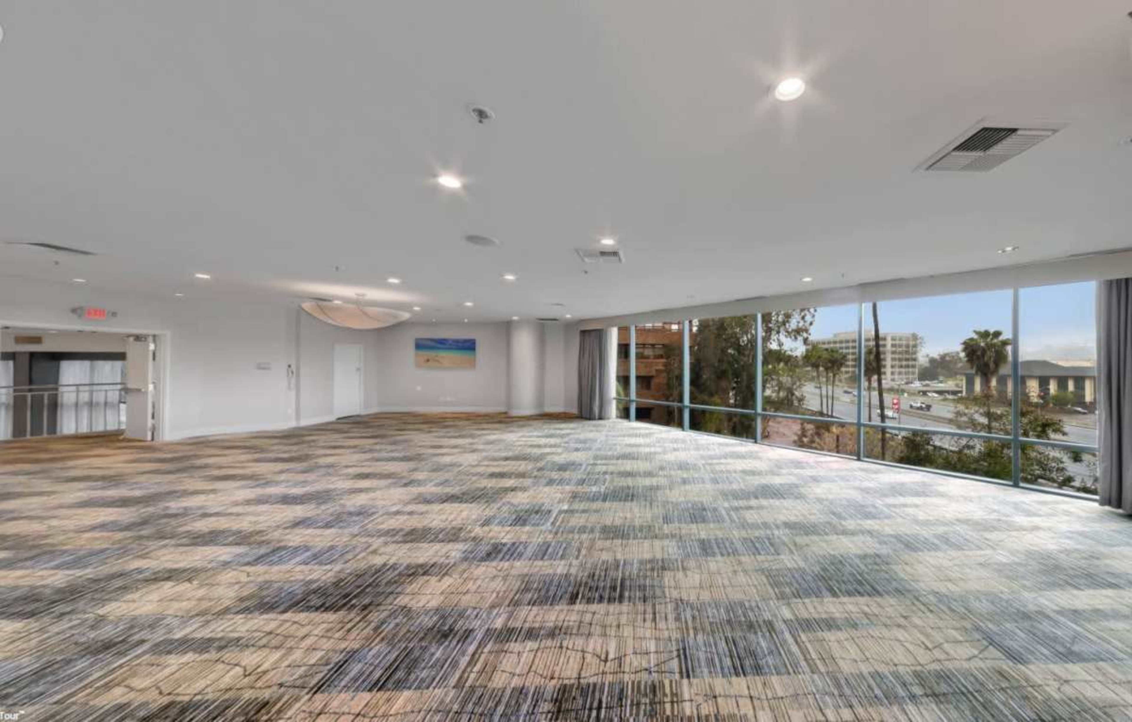 The image shows an empty, well-lit conference room with large windows and a patterned carpet.