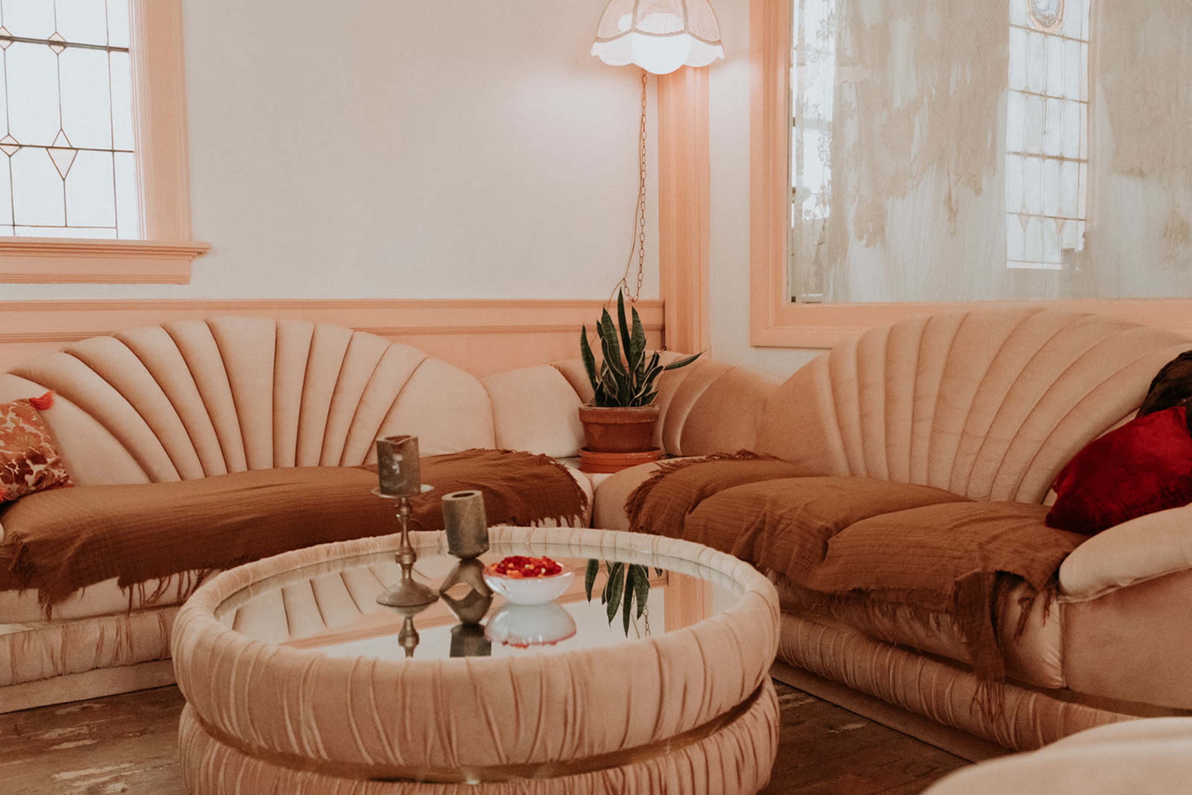 The image shows a cozy living room with two curved, upholstered sofas, a round glass coffee table, and a potted plant.