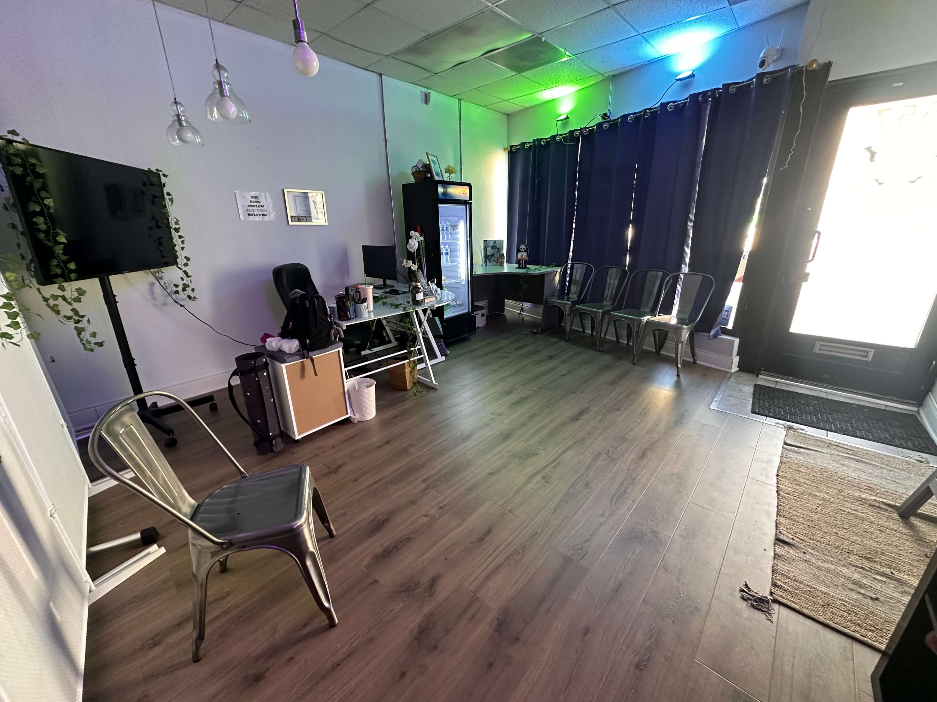 The image shows a sparsely furnished room with chairs arranged against the wall, a table with equipment, and a door leading outside.