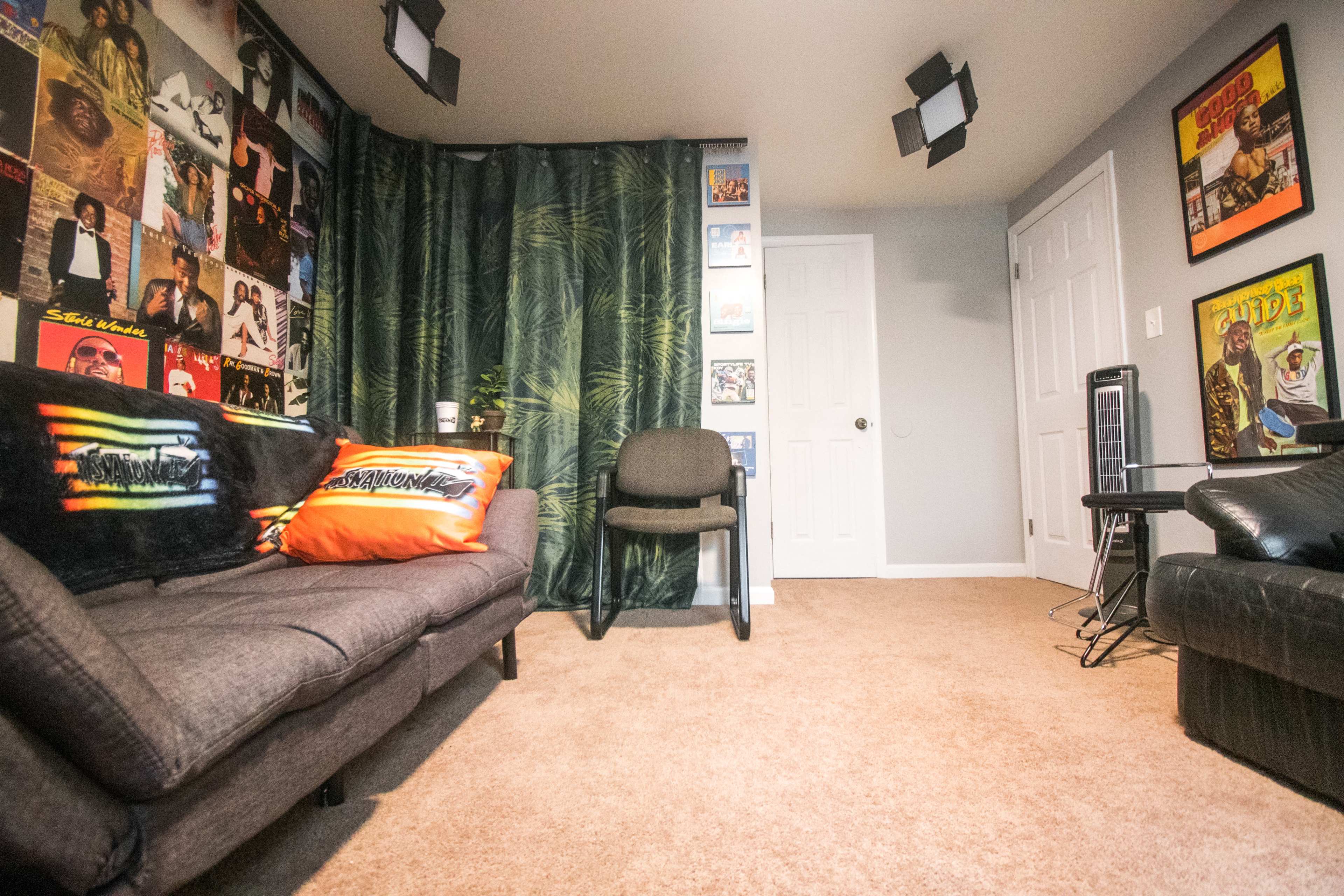 A room with a couch, a chair, and walls adorned with album covers and a green curtain, creating a cozy space.